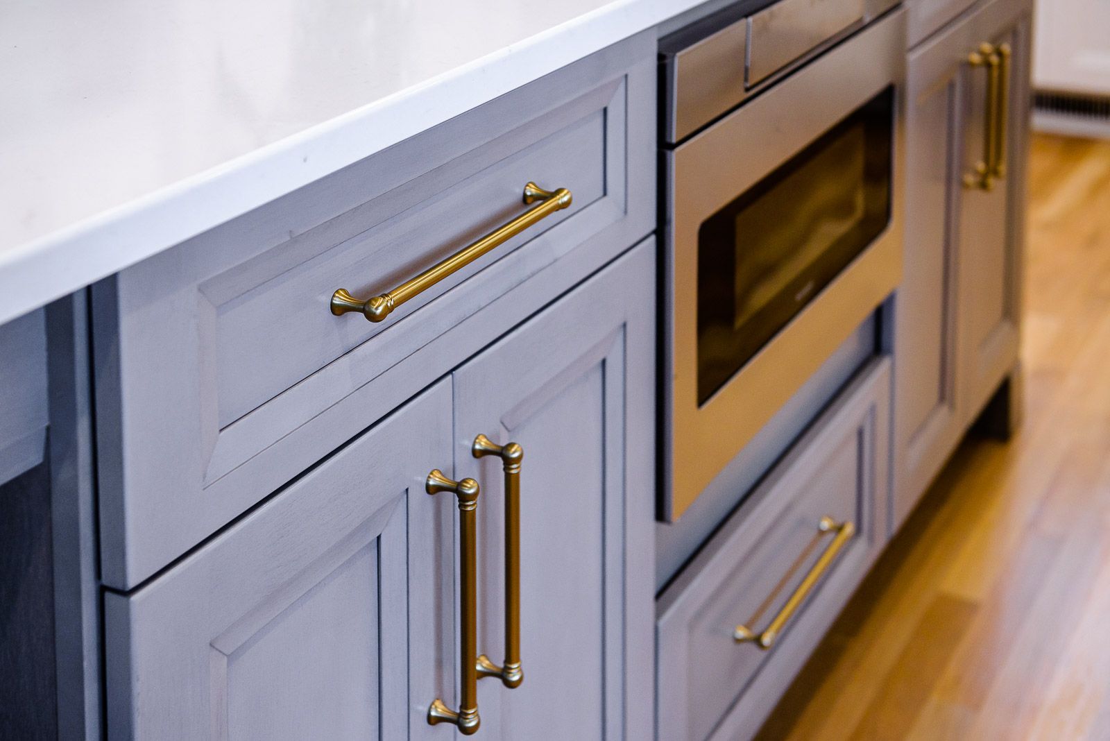 A kitchen with gray cabinets and gold handles and a stainless steel oven.