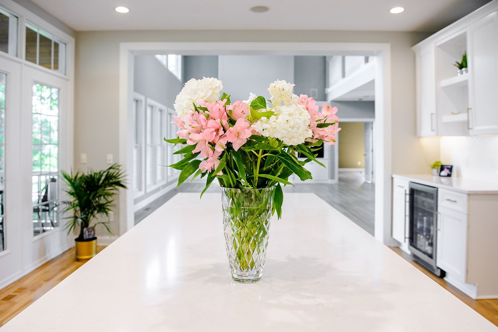A vase filled with pink and white flowers is on a counter in a kitchen.