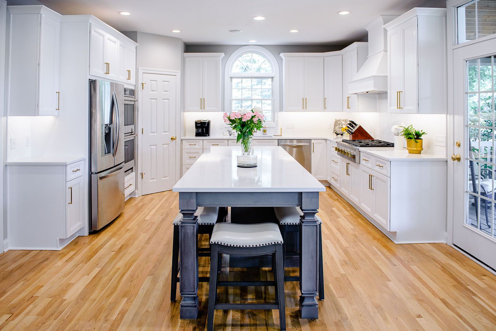 A kitchen with white cabinets , stainless steel appliances , hardwood floors and a large island.