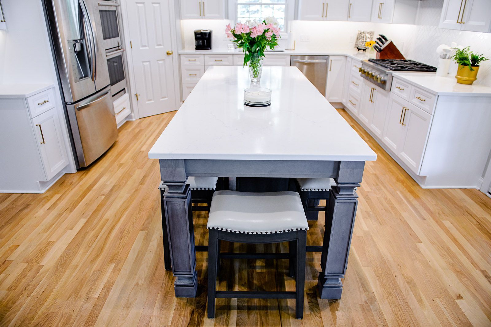 There is a large island in the middle of the kitchen with a vase of flowers on it.