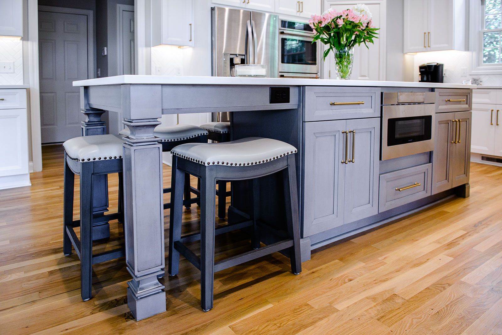 A kitchen with a large island and stools and a vase of flowers on the counter.
