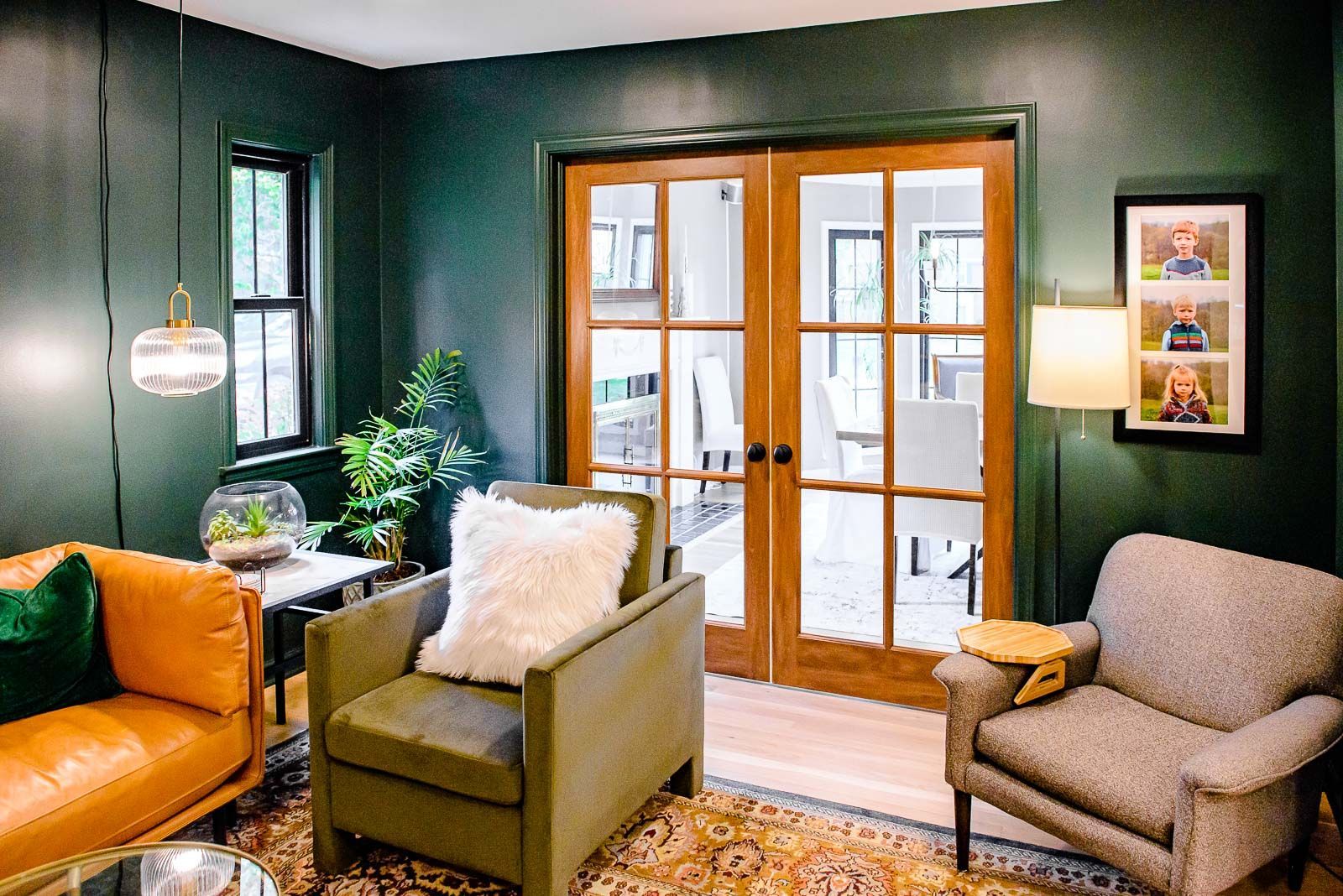 A living room with green walls , two chairs , a couch and a lamp.