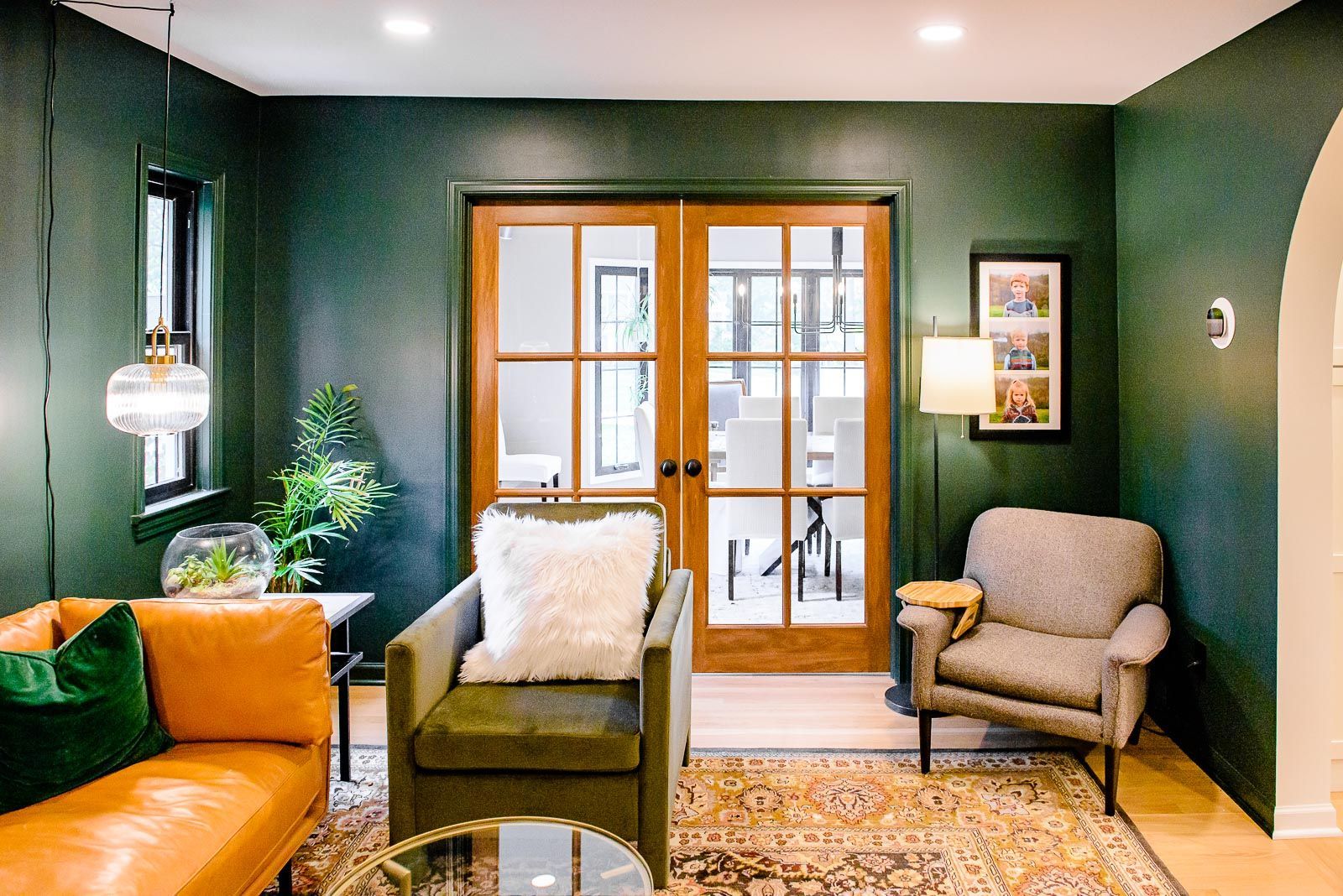 A living room with green walls , a couch , chairs , and a rug.