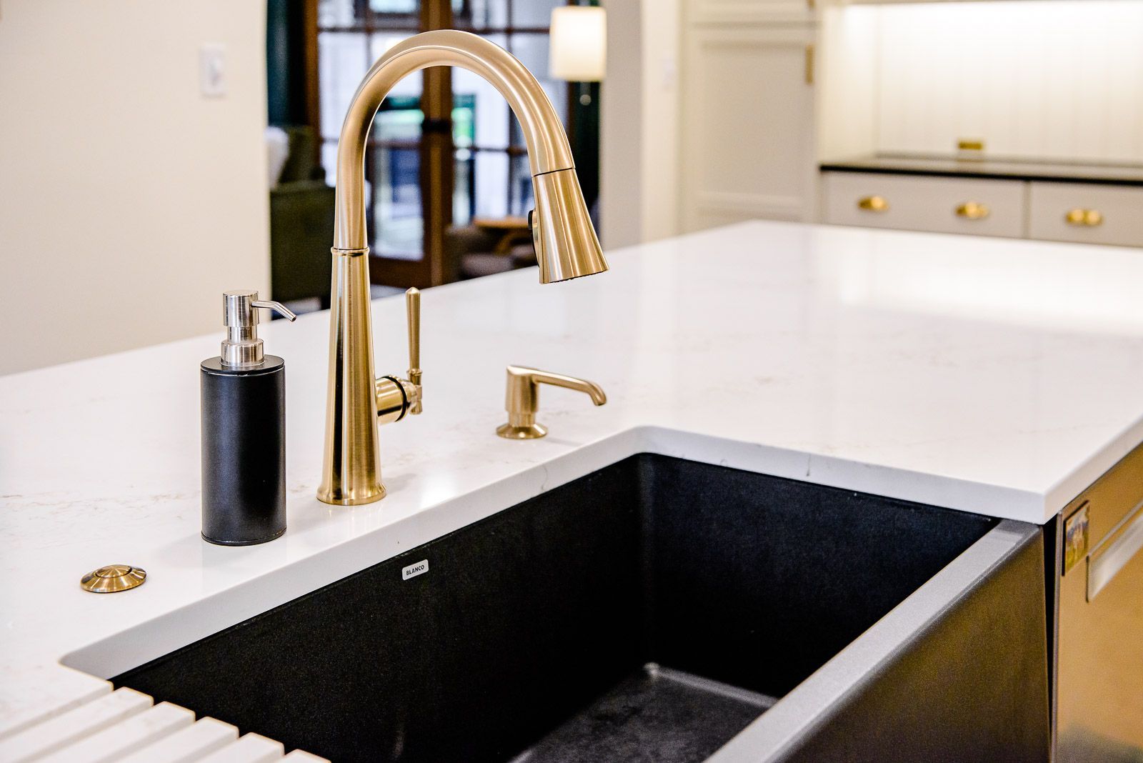 A kitchen sink with a gold faucet and soap dispenser on the counter.