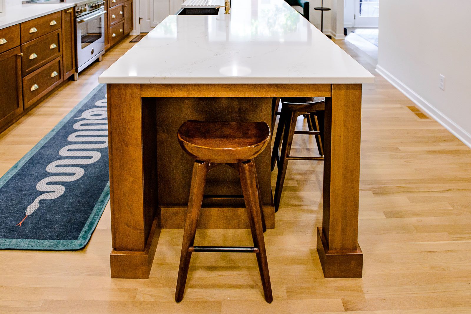 A wooden stool is sitting under a long wooden table in a kitchen.