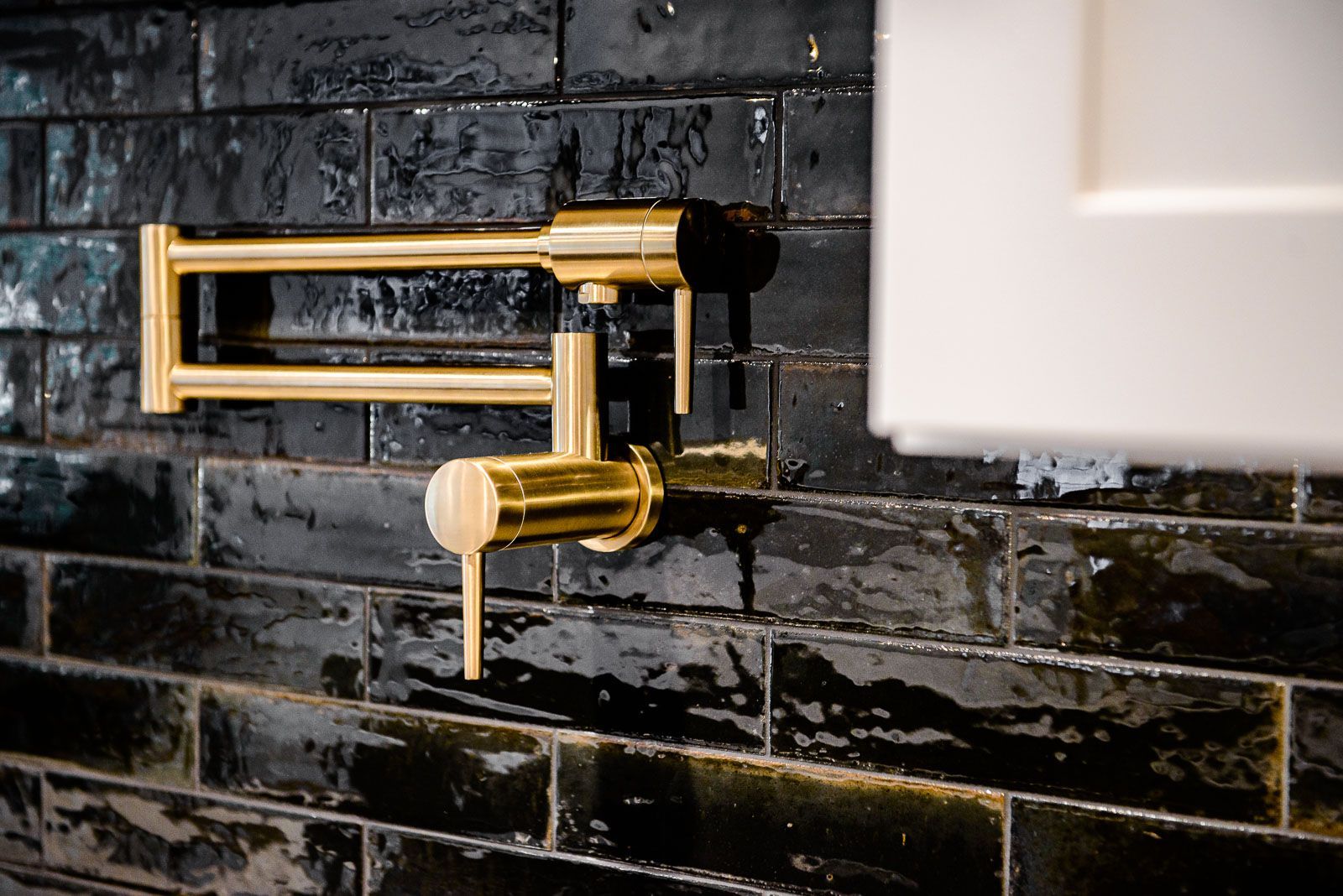 A gold faucet is hanging on a black brick wall.