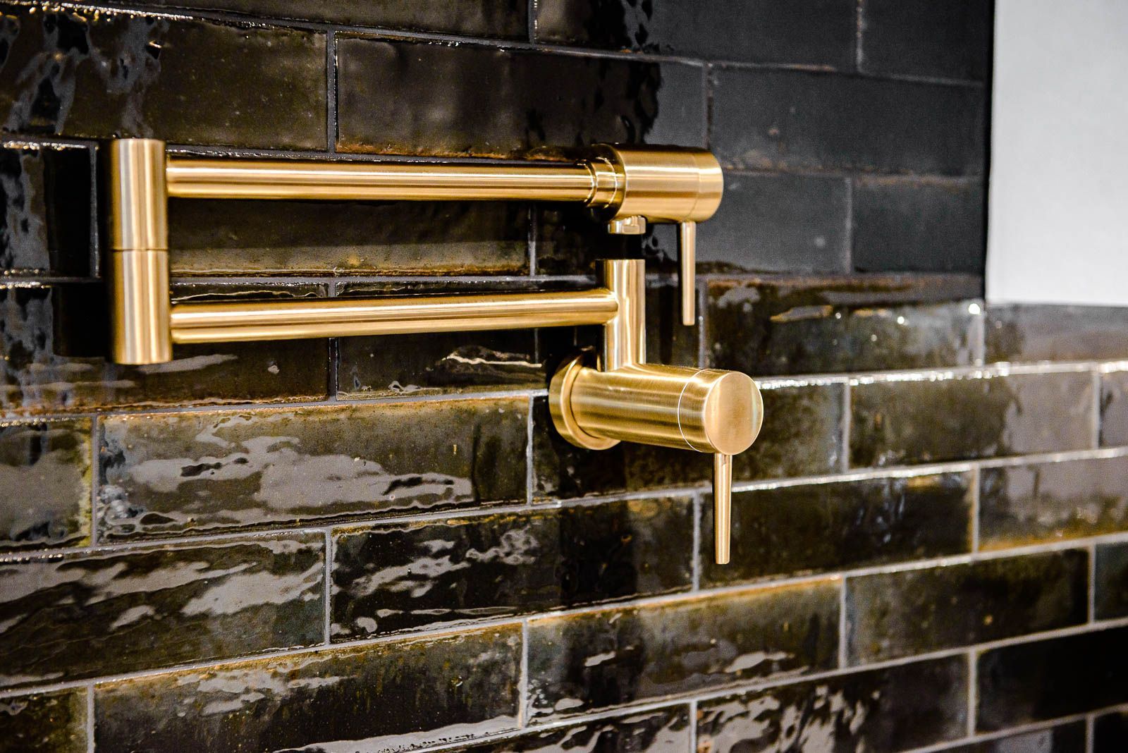 A gold faucet is hanging on a black tiled wall.