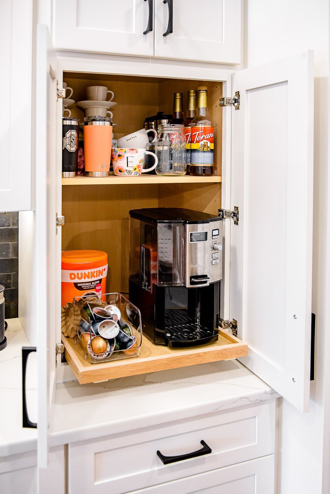 A coffee maker is sitting inside of a cabinet in a kitchen.