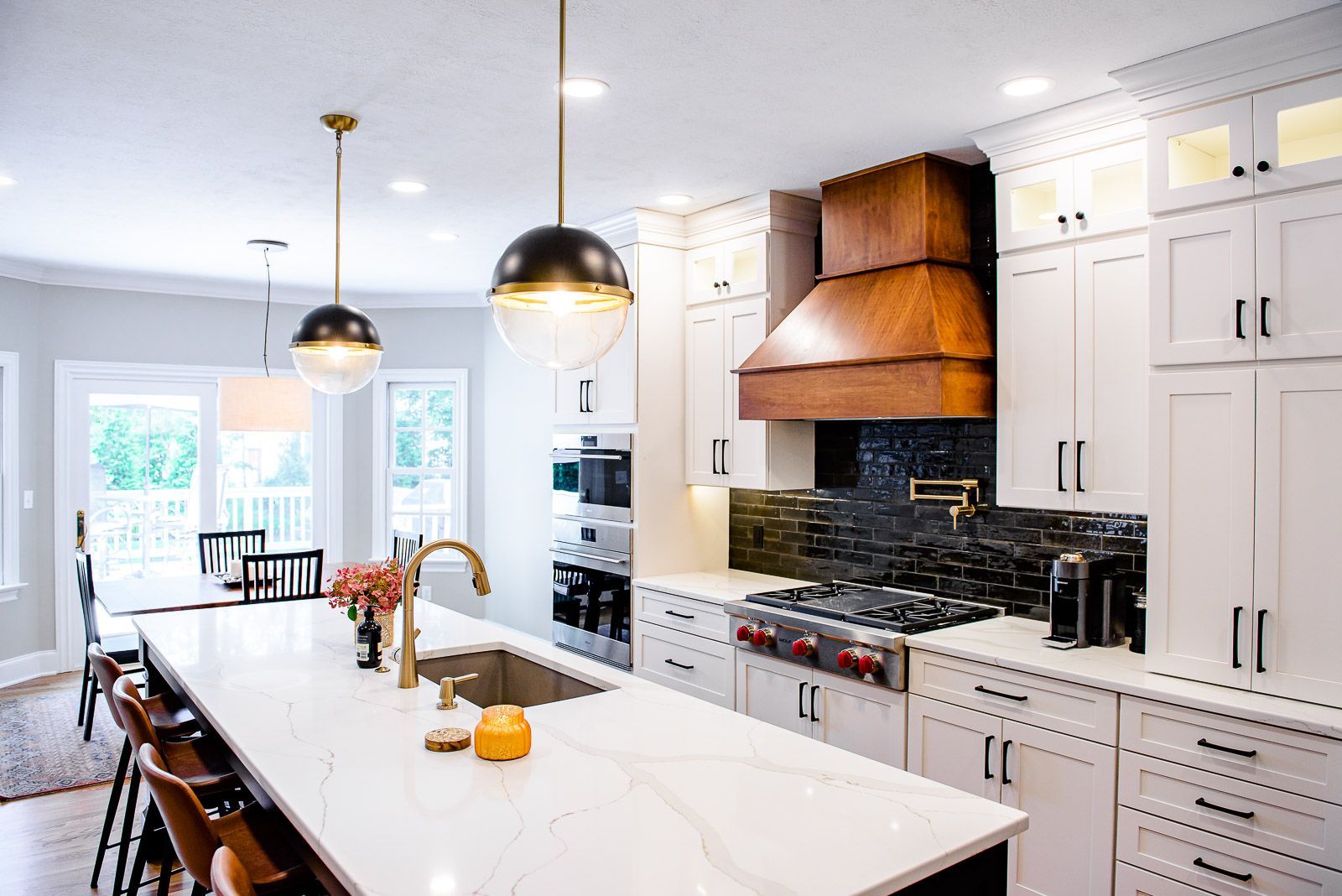 A kitchen with white cabinets , a large island , a stove , a sink , and a hood.