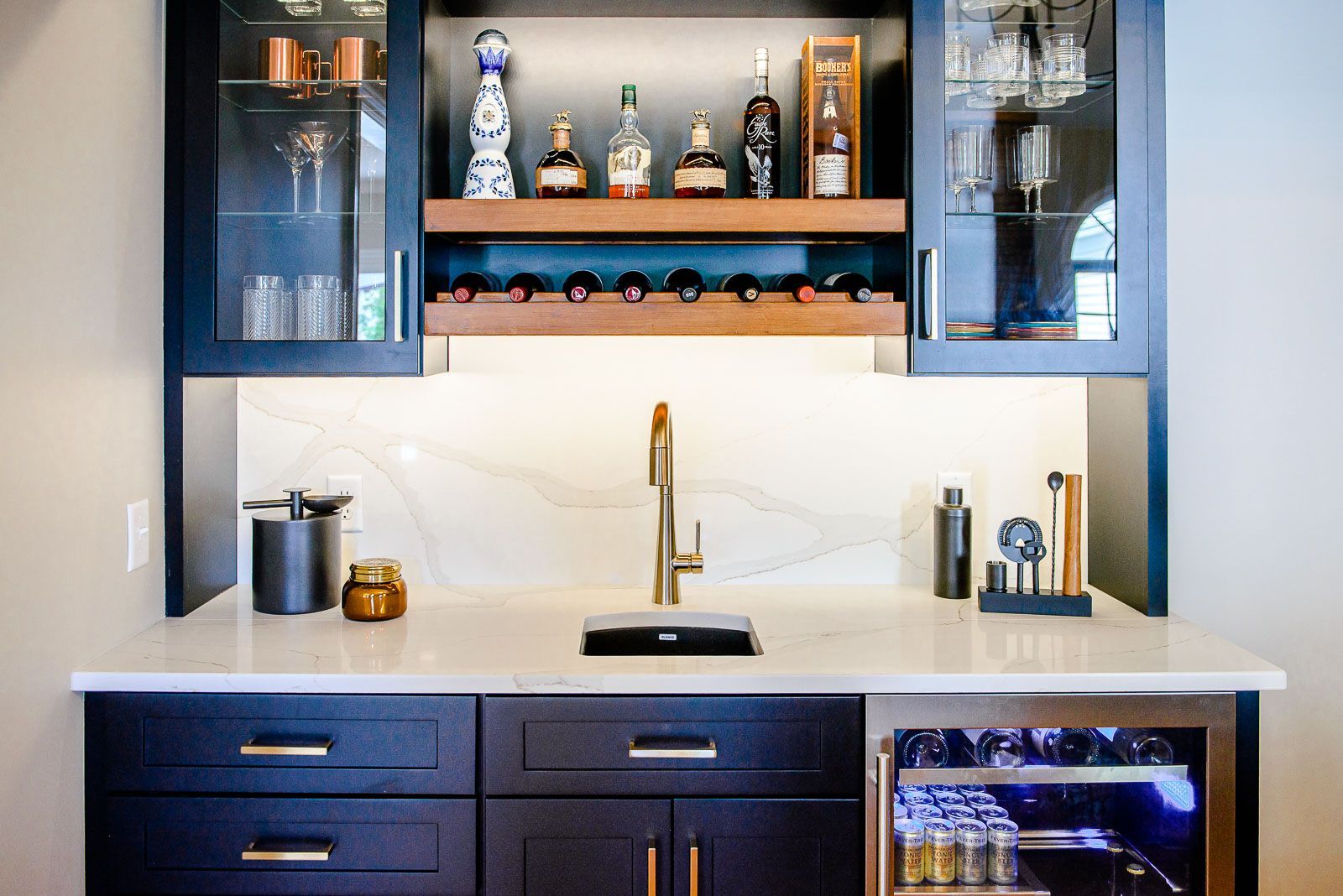 A kitchen with a sink , a refrigerator , a bottle rack , and a wine cooler.