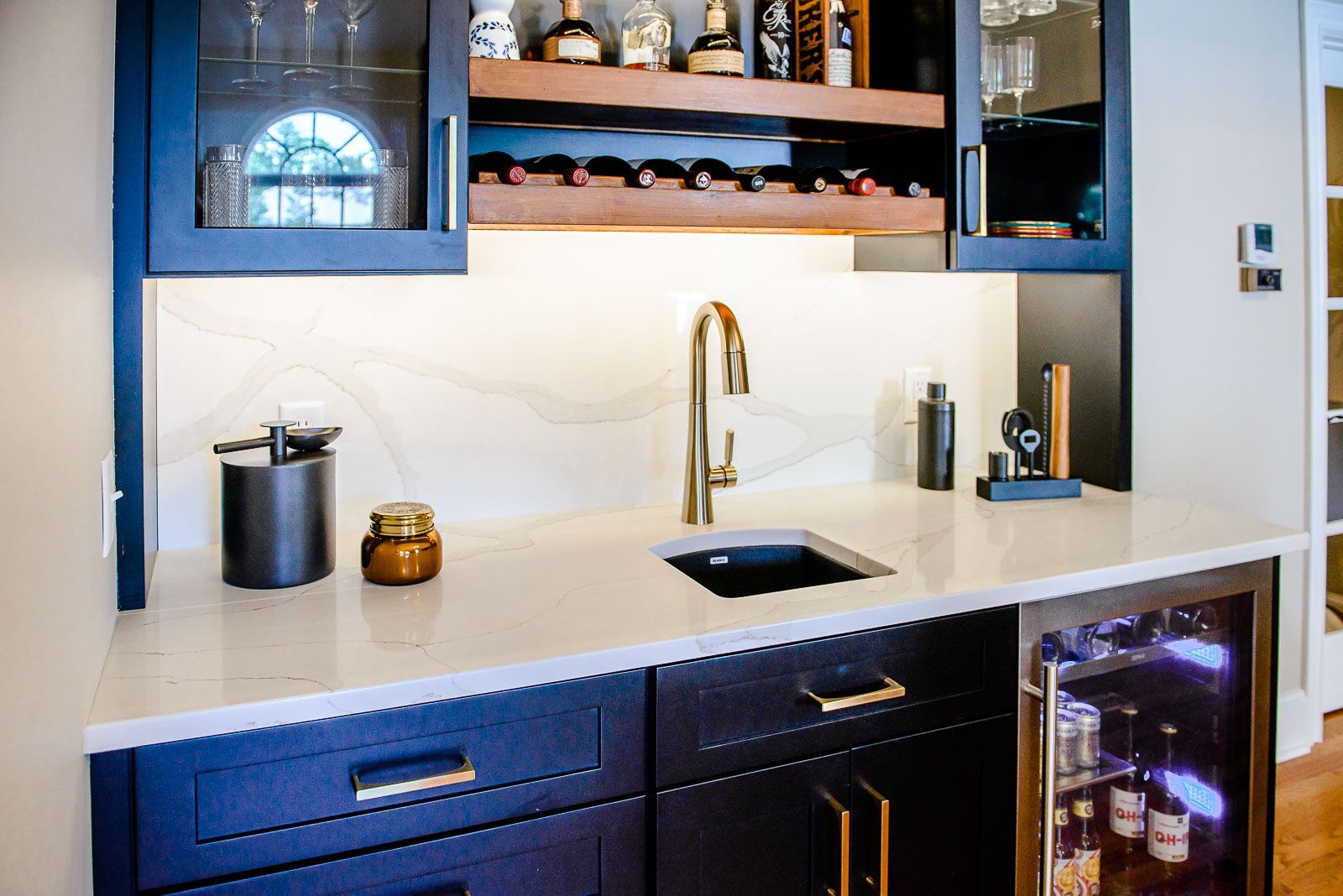 A kitchen with blue cabinets , a sink , a refrigerator and a wine rack.