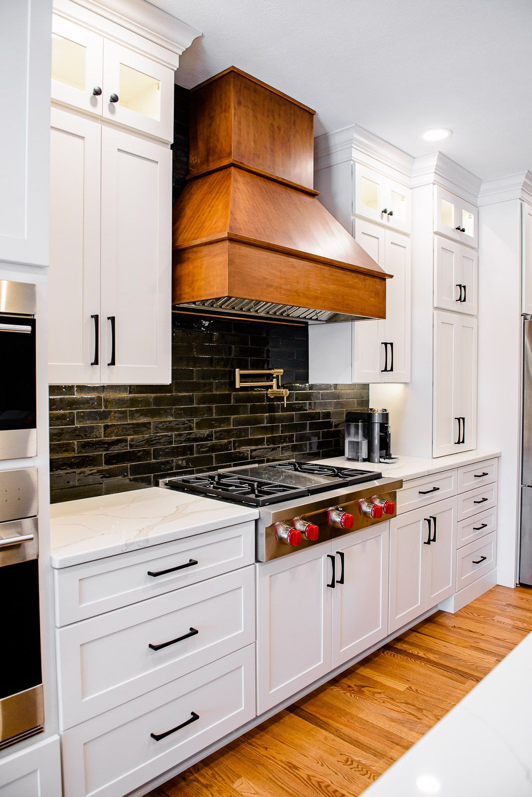 A kitchen with white cabinets , stainless steel appliances , and a wooden hood above the stove.