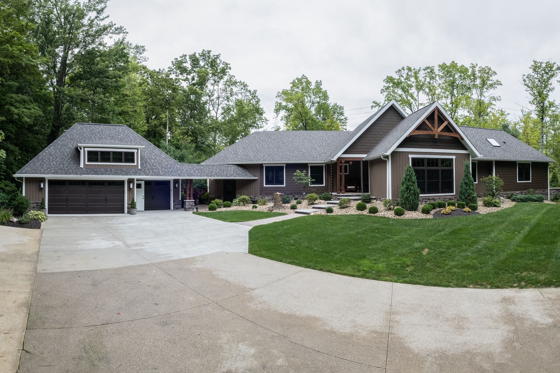 Brown ranch-style house with gray roof and attached garage on a large lawn with a circular driveway.
