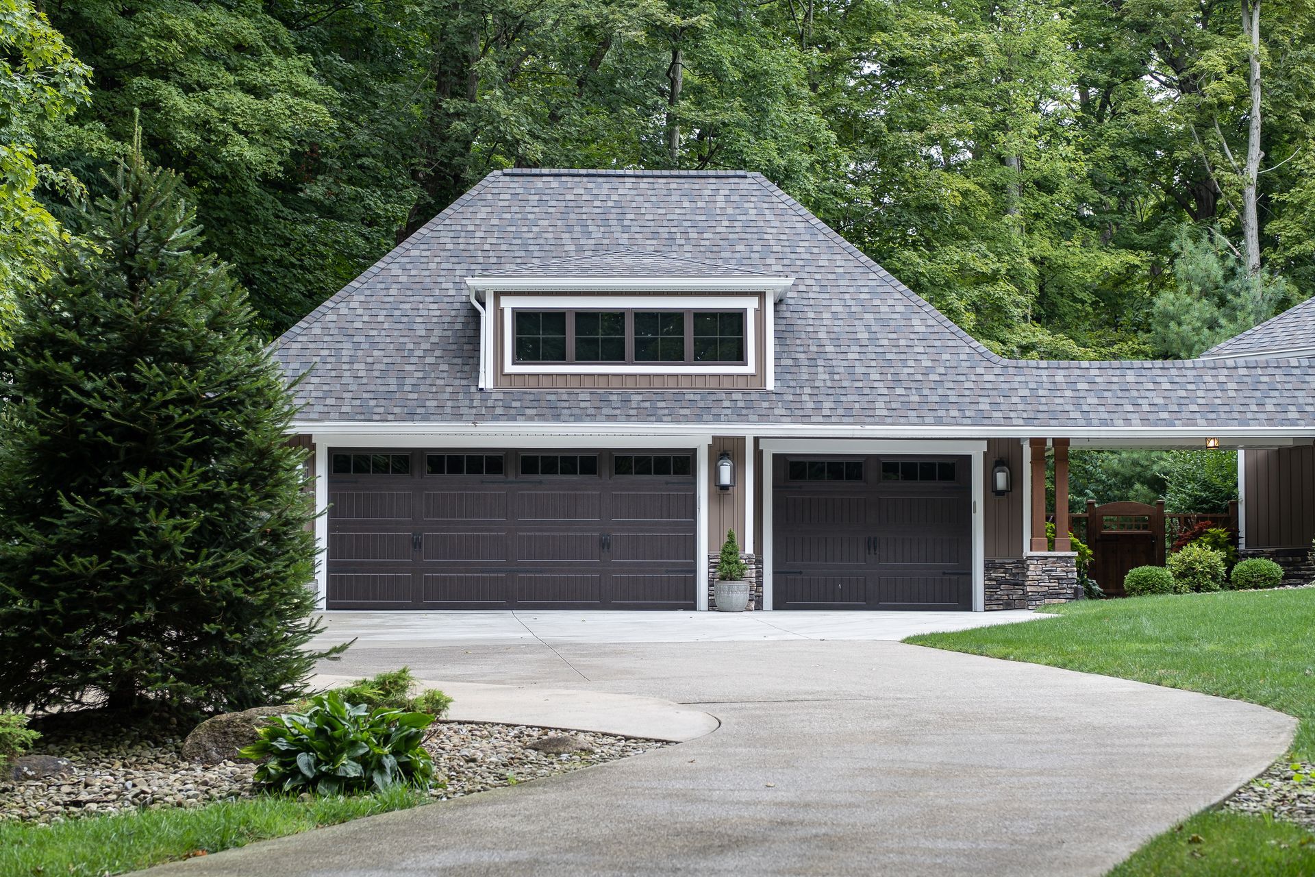 Brown garage with two doors, tan siding, and a winding driveway, set against a green forest.