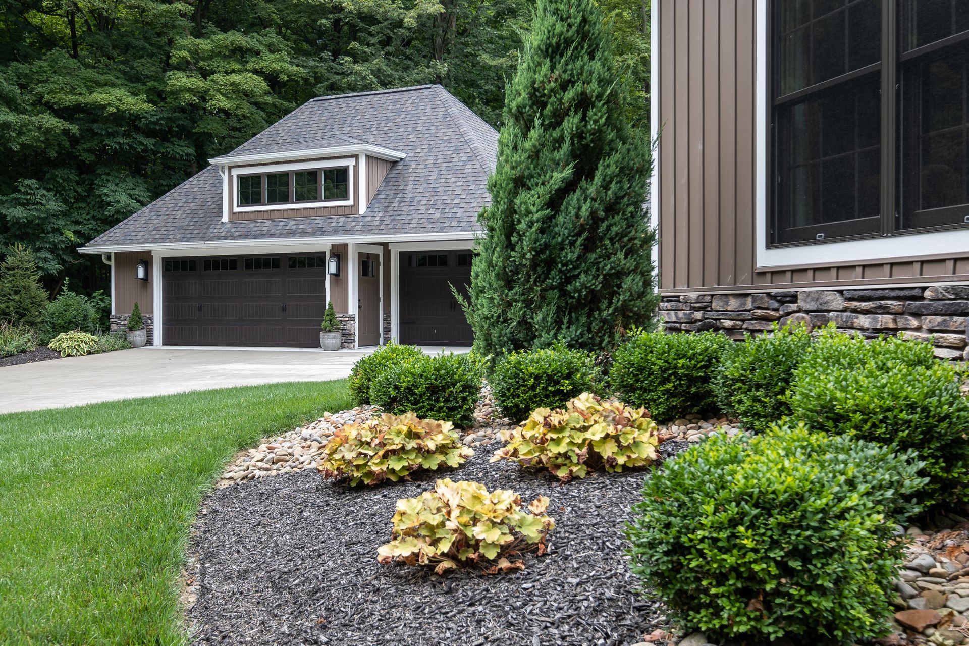 Landscaped front yard with a brown garage and a house with stone siding.