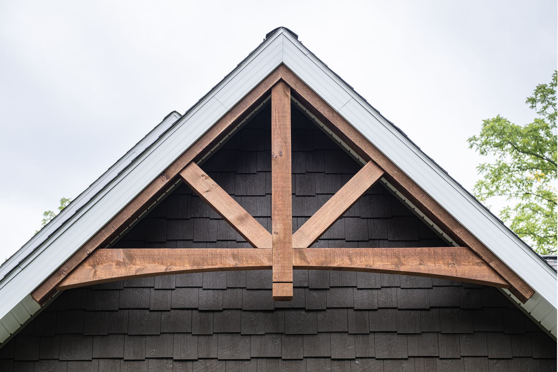 Brown wooden decorative gable trim on a dark shingled building against a cloudy sky.