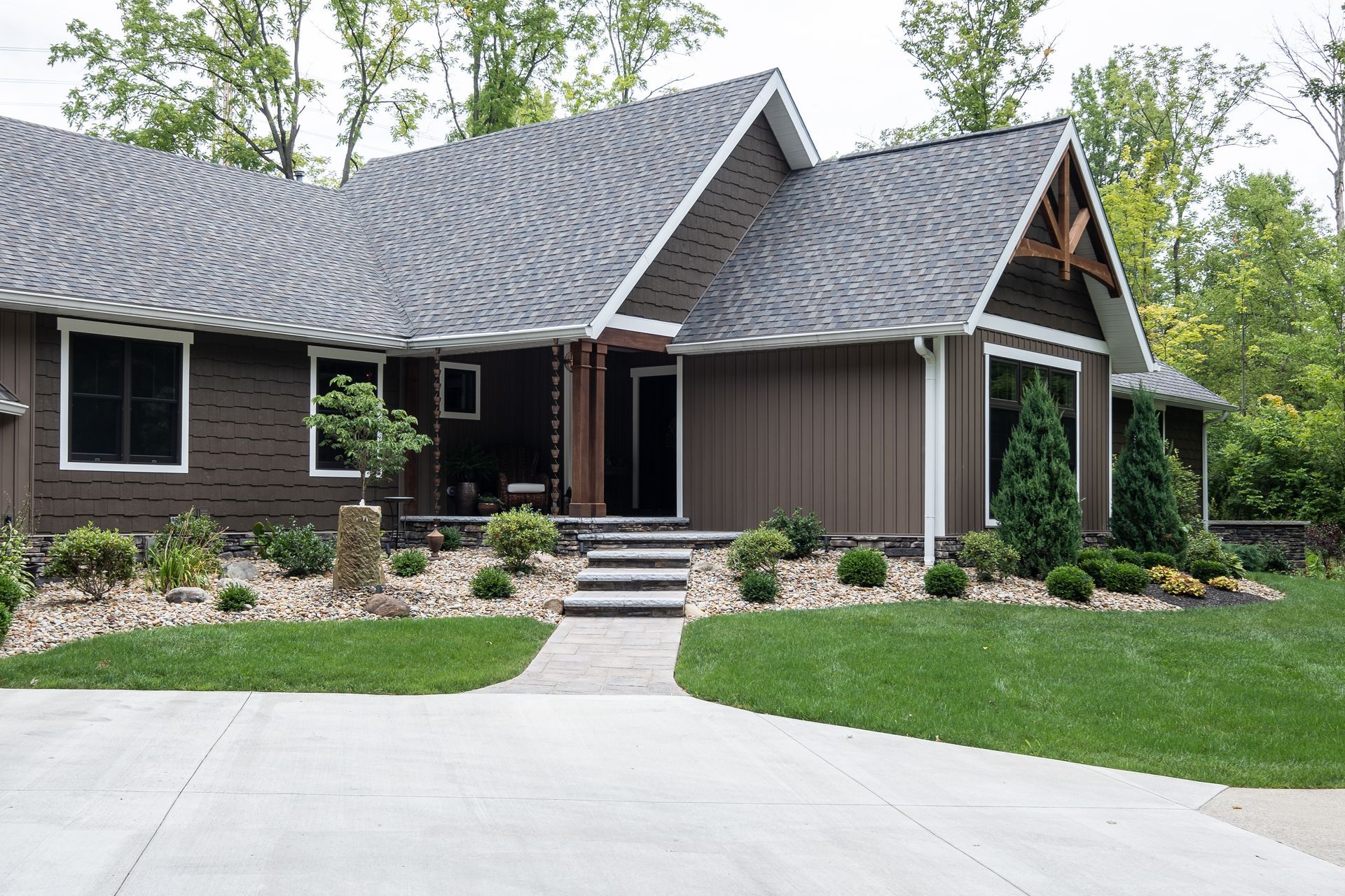 Brown house with gray roof, small shrubs, and a concrete path.
