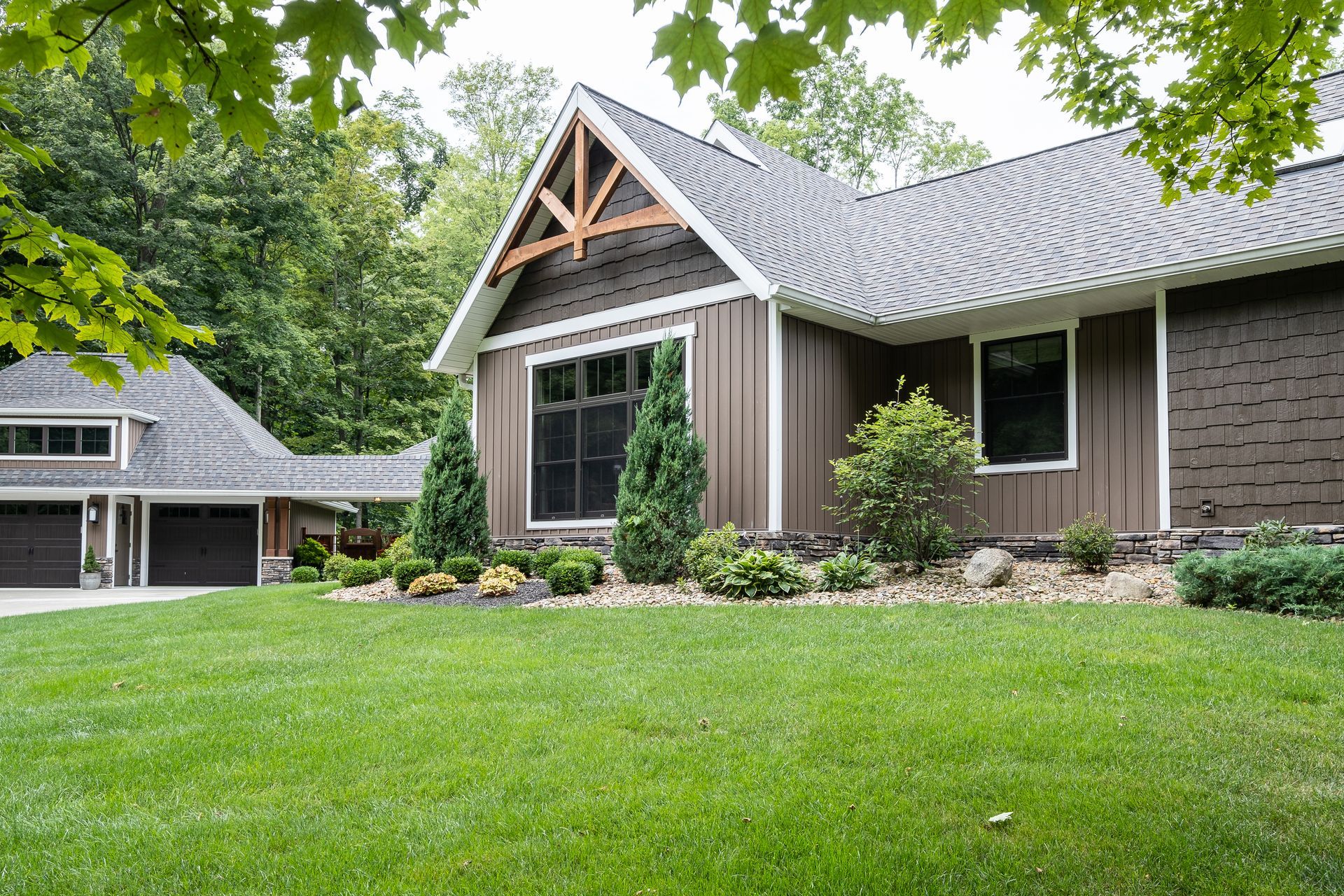 Brown house with gray roof, green lawn, trees, and a detached garage.