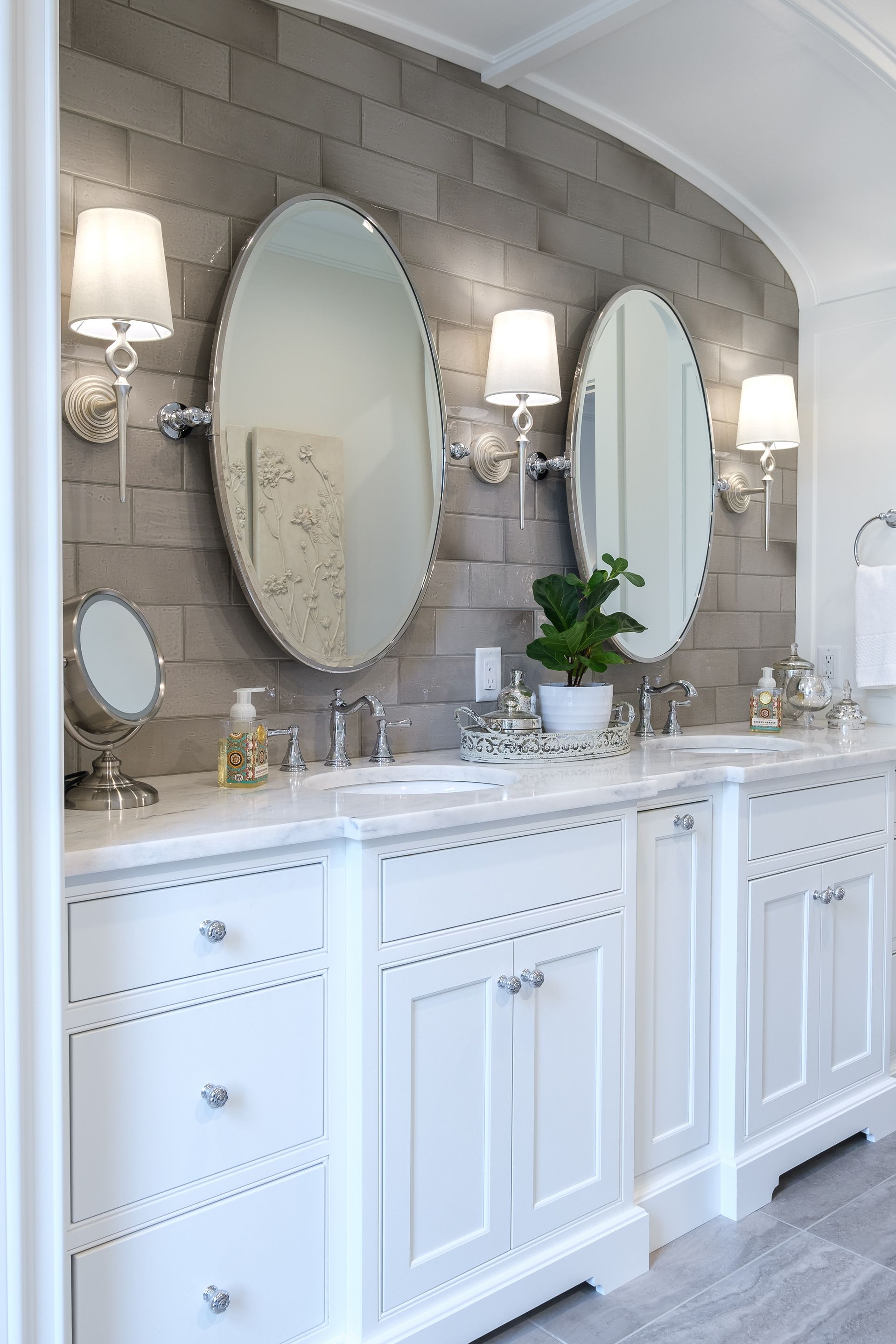 White double vanity with oval mirrors, sconces, and gray tiled accent wall.