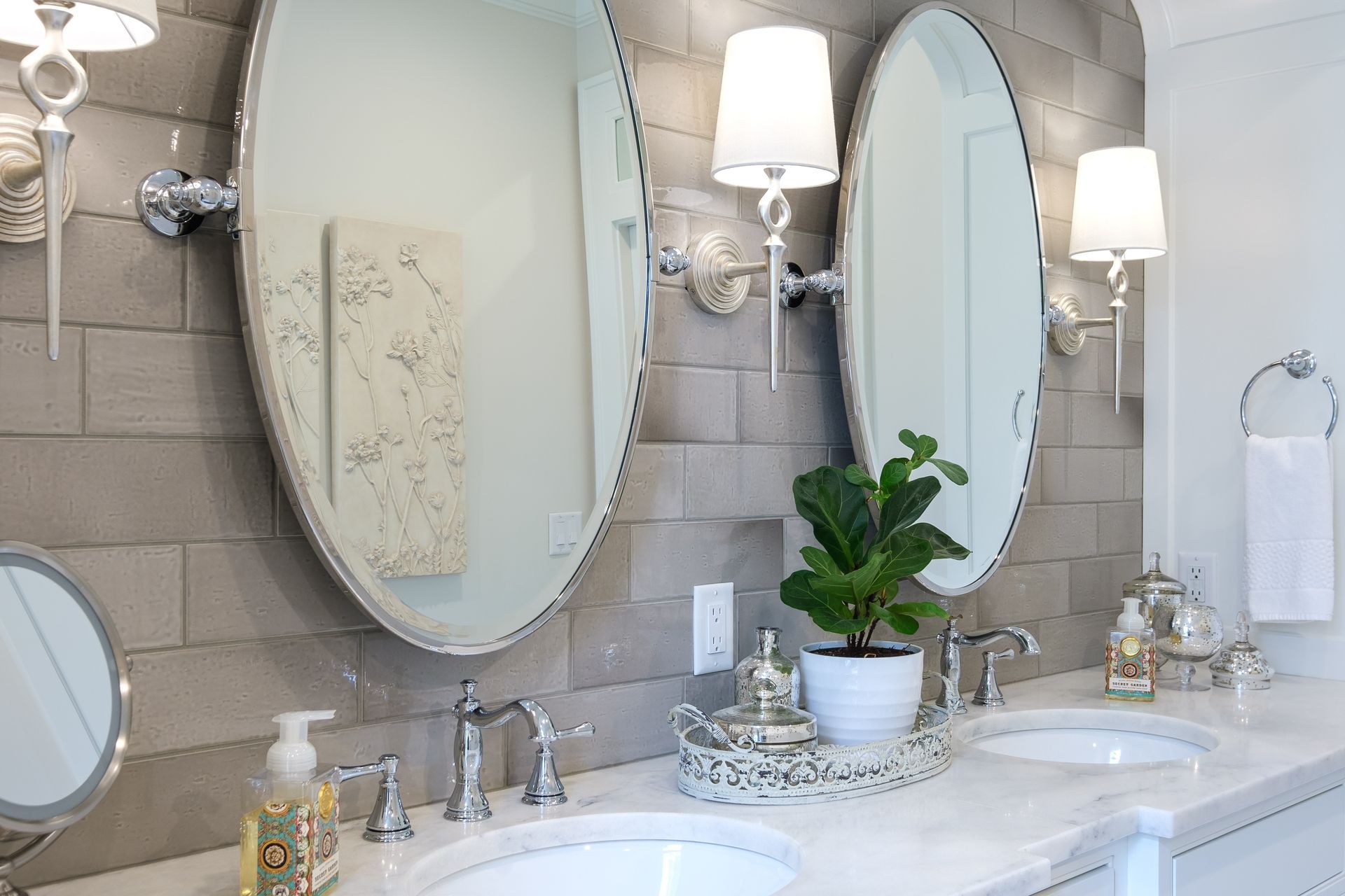 Bathroom with oval mirrors, gray brick wall, and white marble countertop.