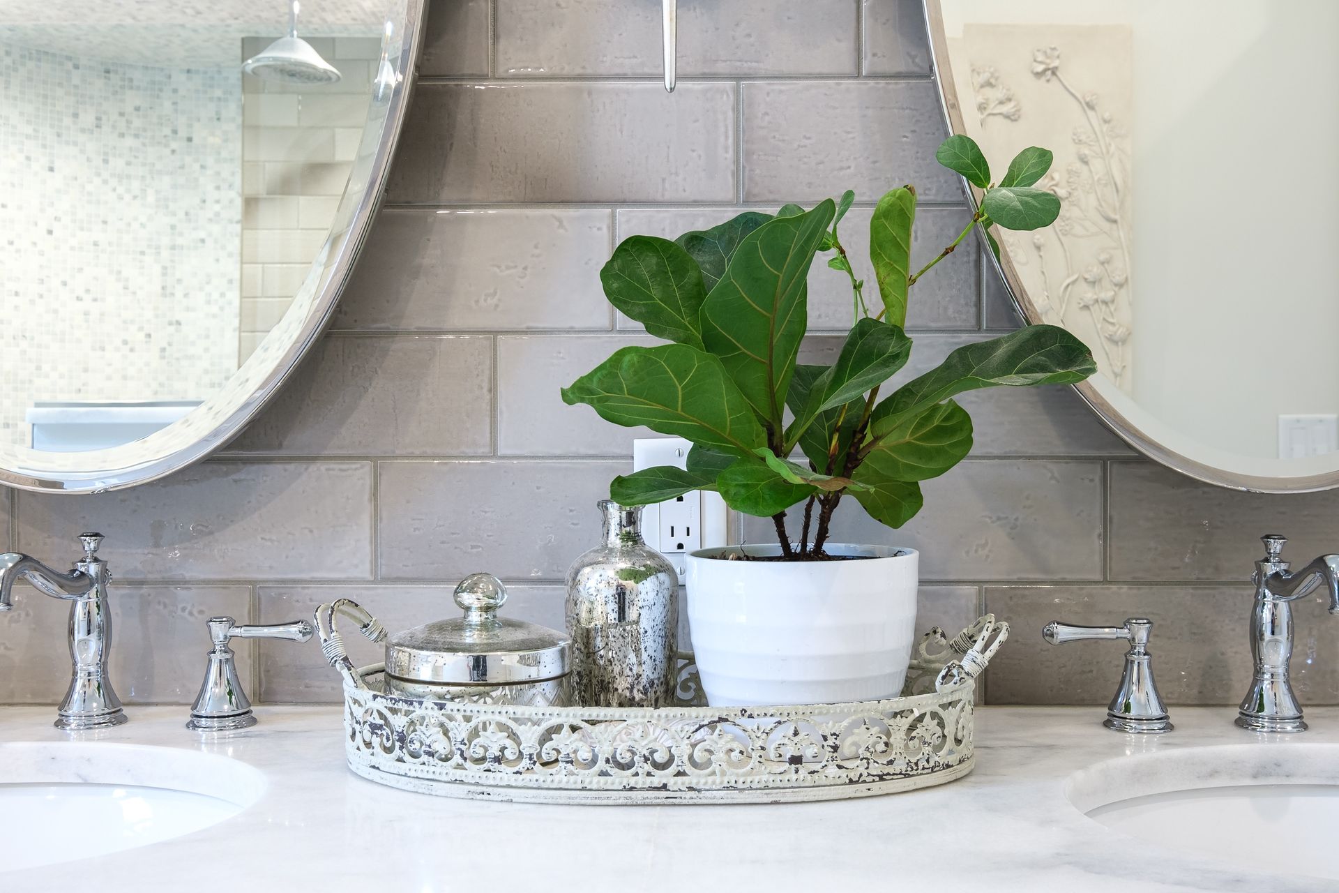 Bathroom vanity with oval mirrors, a plant, and decorative tray on a white countertop.