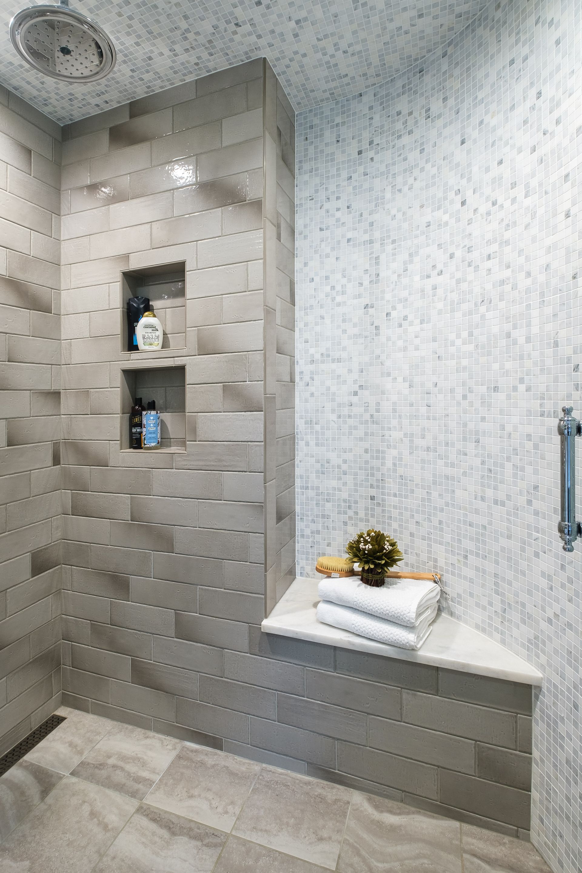 Modern shower with gray tile, built-in shelves, a bench, and a round rain shower head.