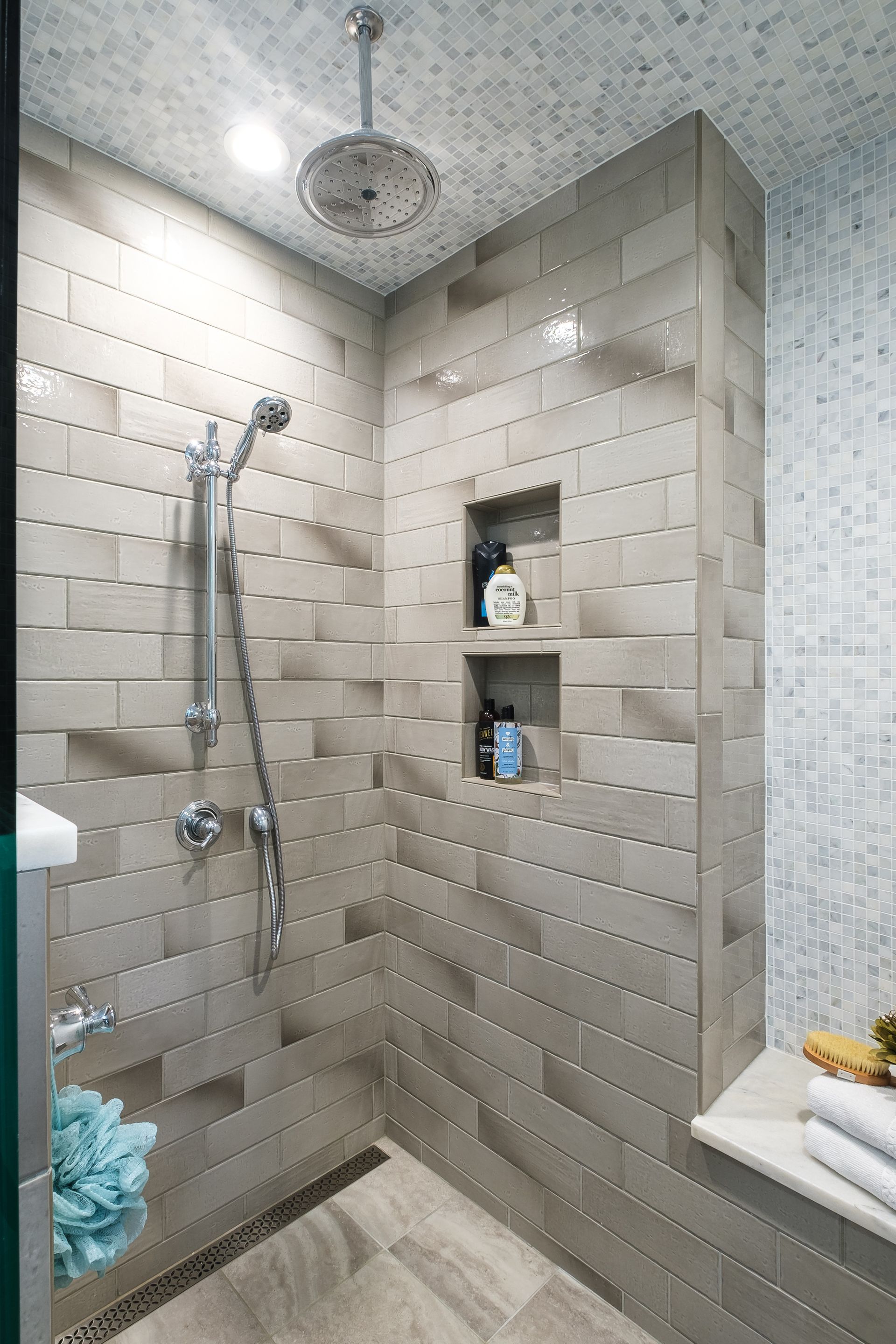 Modern walk-in shower with gray tiled walls and two built-in shelves. Silver showerhead and handheld wand.