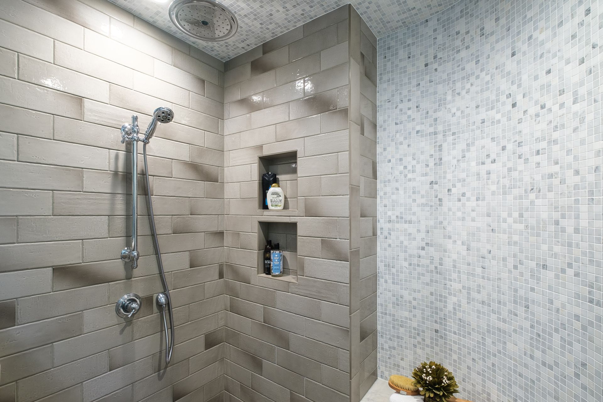 Gray tiled shower with a built-in shelf holding toiletries, a showerhead, and handheld shower.