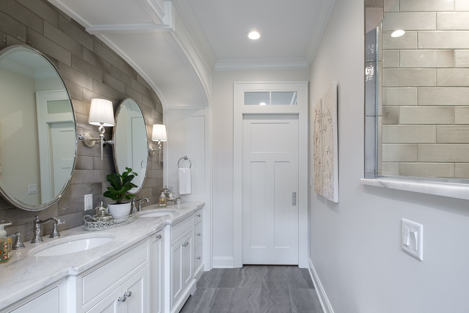 Bathroom with white vanity, gray brick wall, mirrors, and door.