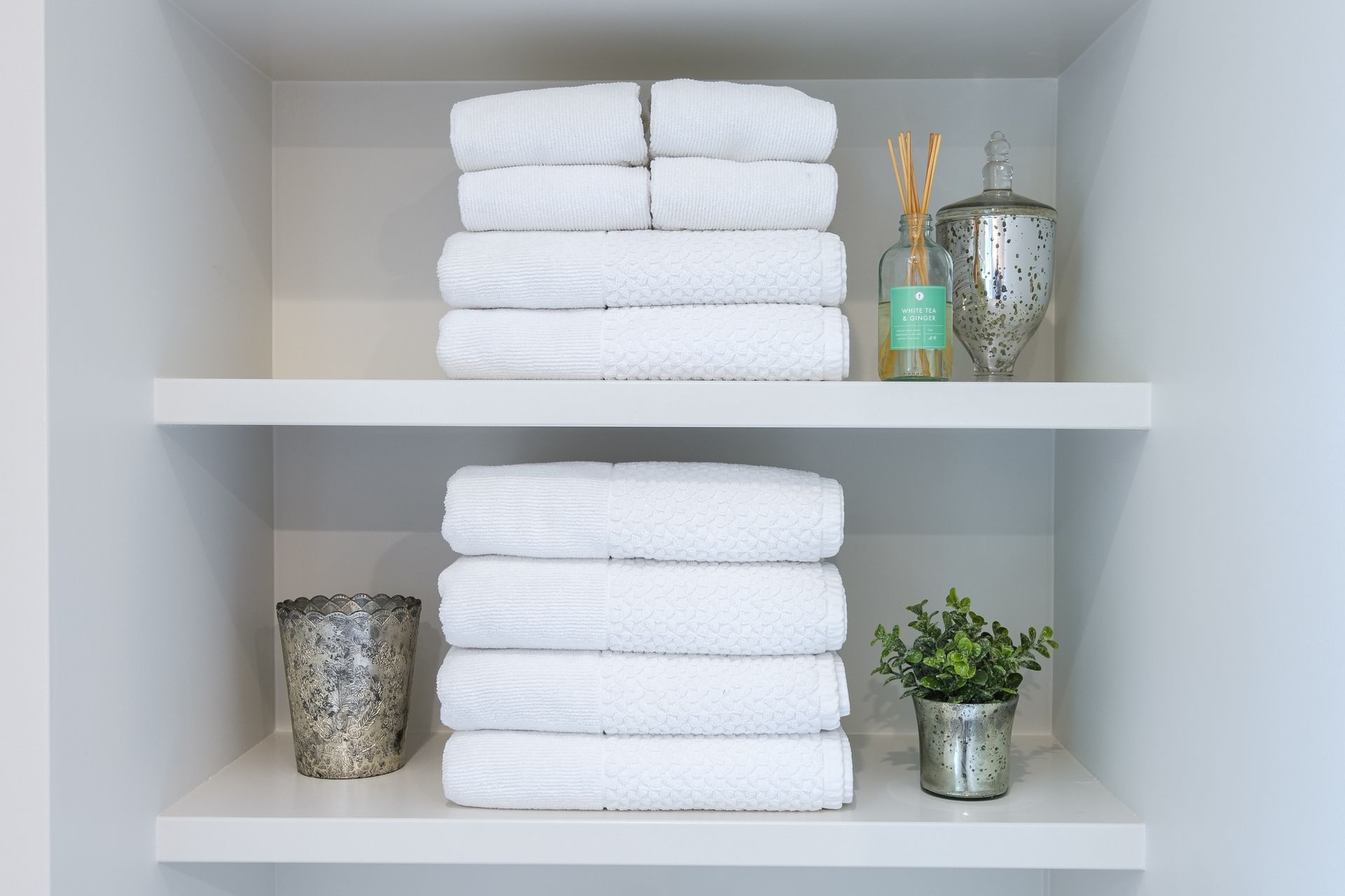 White towels stacked neatly on shelves, with decorative items like diffusers and plants.
