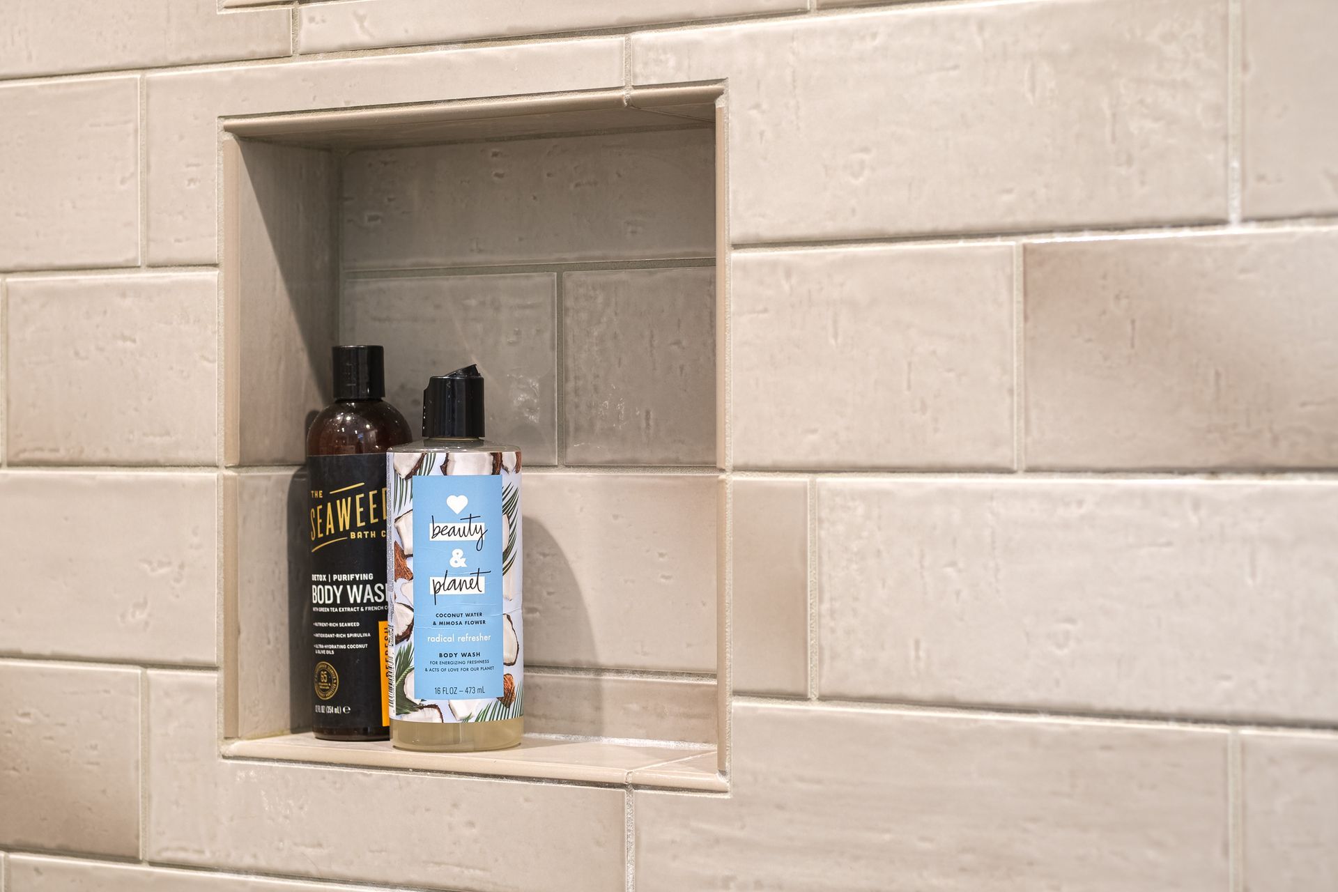 Built-in shower shelf with shampoo and conditioner bottles, against a light-colored tiled wall.