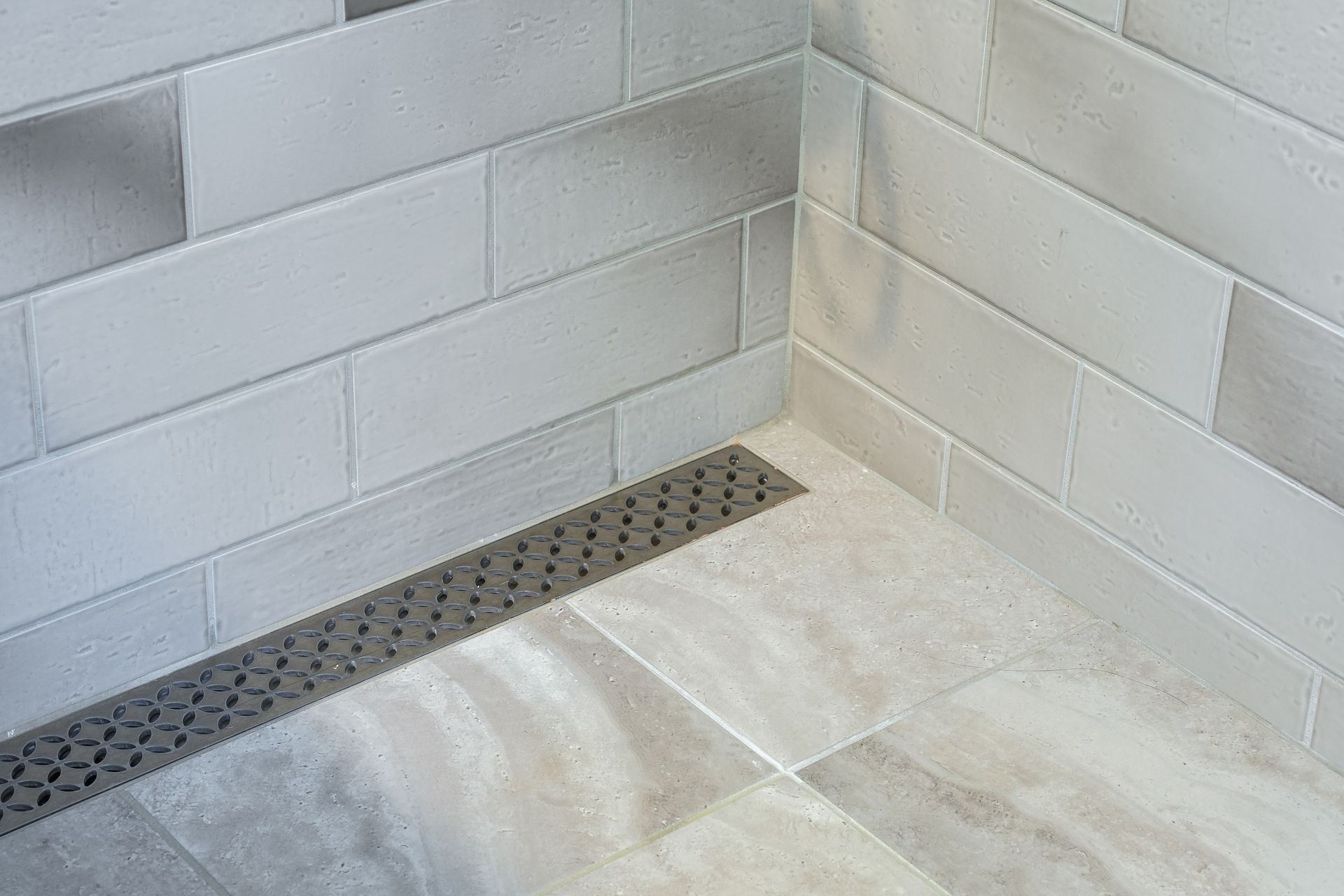 Corner shower with white rectangular tiles and a linear drain.