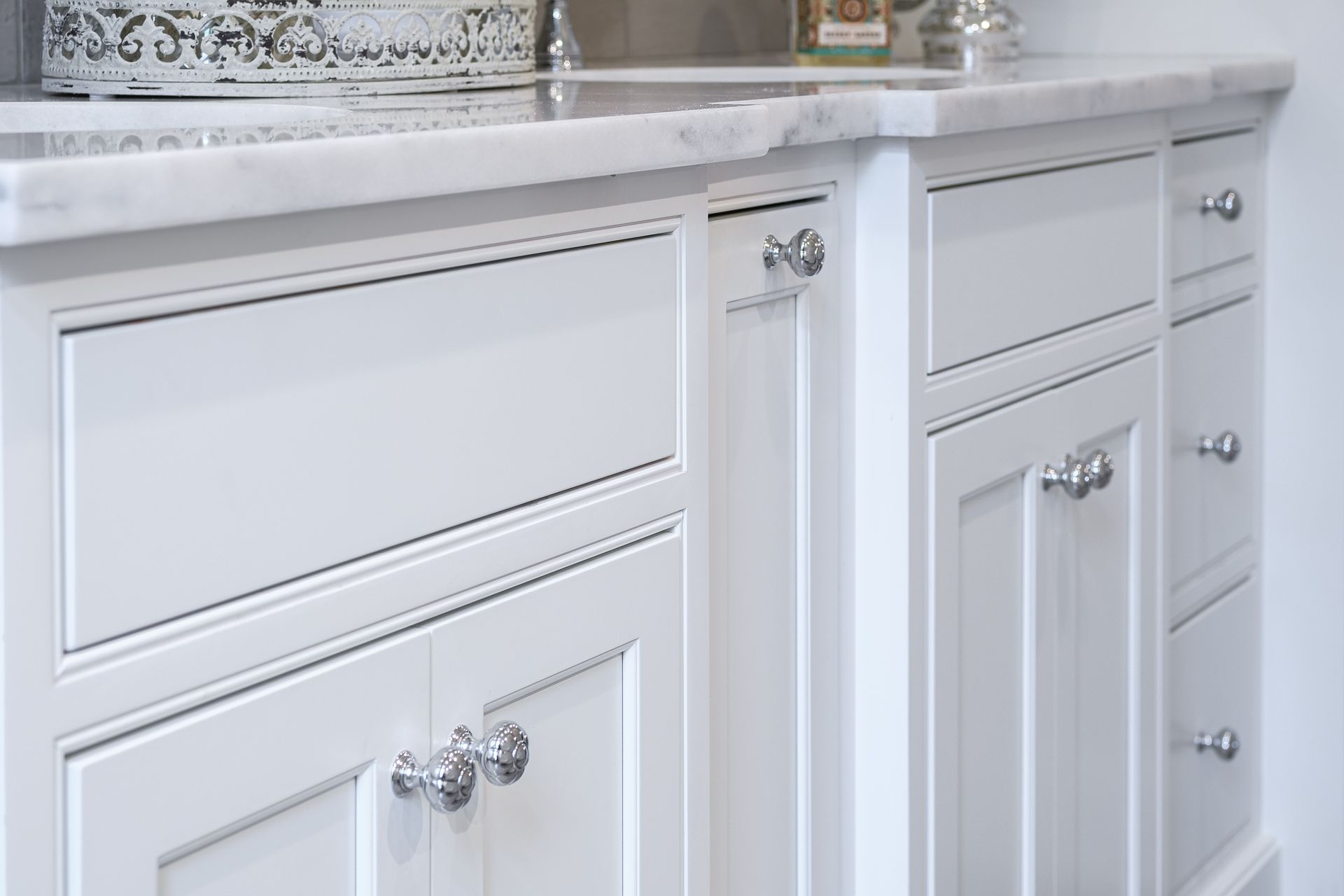 White bathroom vanity with marble countertop and silver knobs.