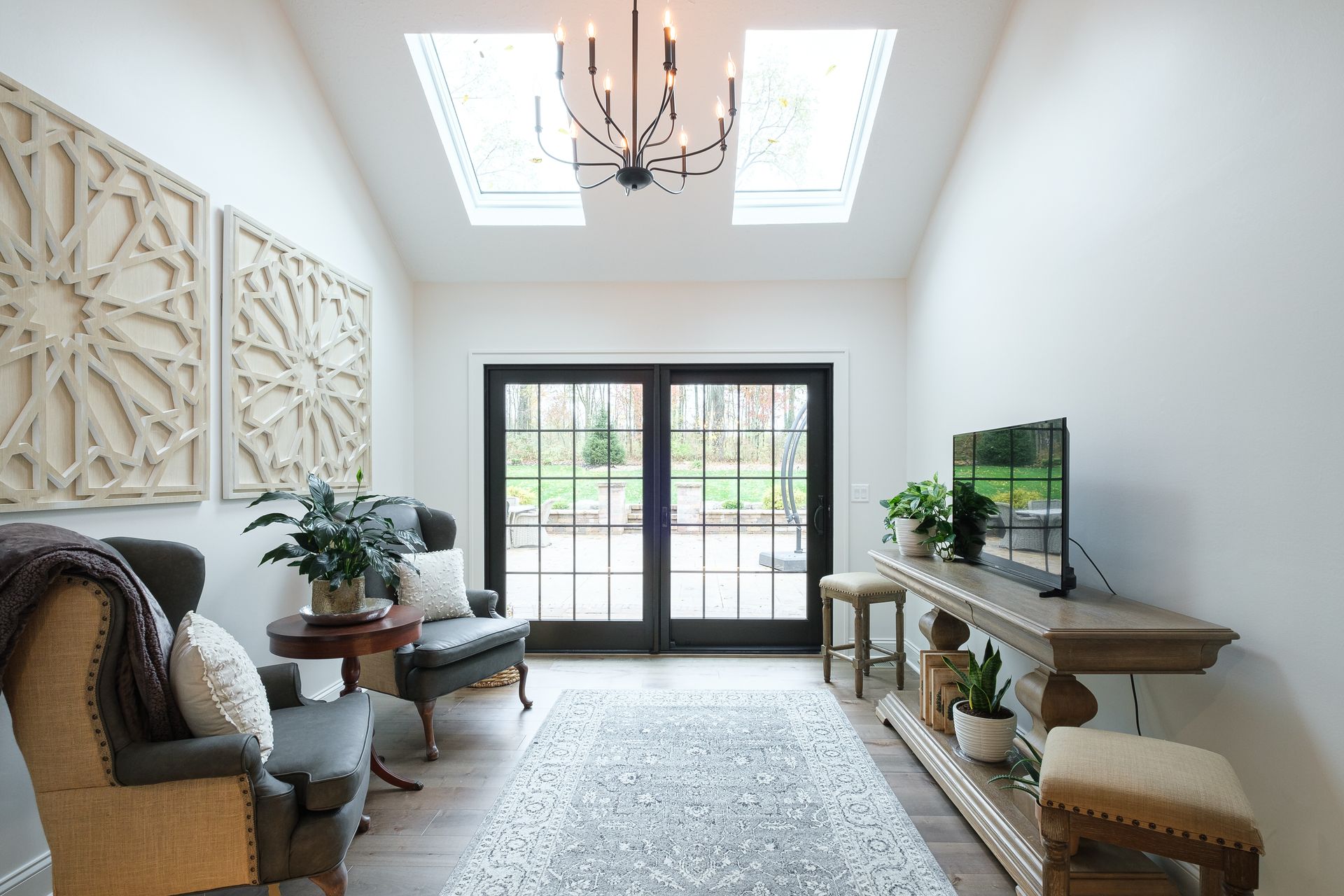 Bright hallway with two skylights, black french doors, seating, and decorative wooden wall panels.