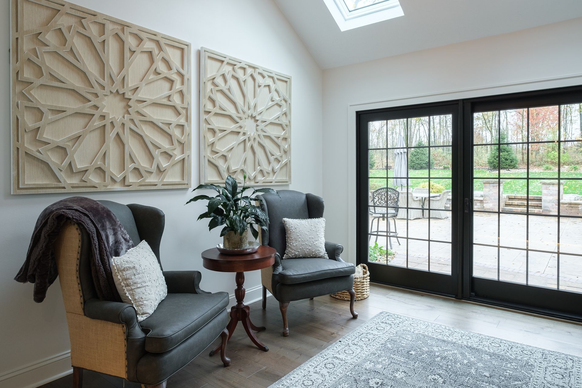 Two gray armchairs flank a small table, below geometric art, by glass doors to a patio.