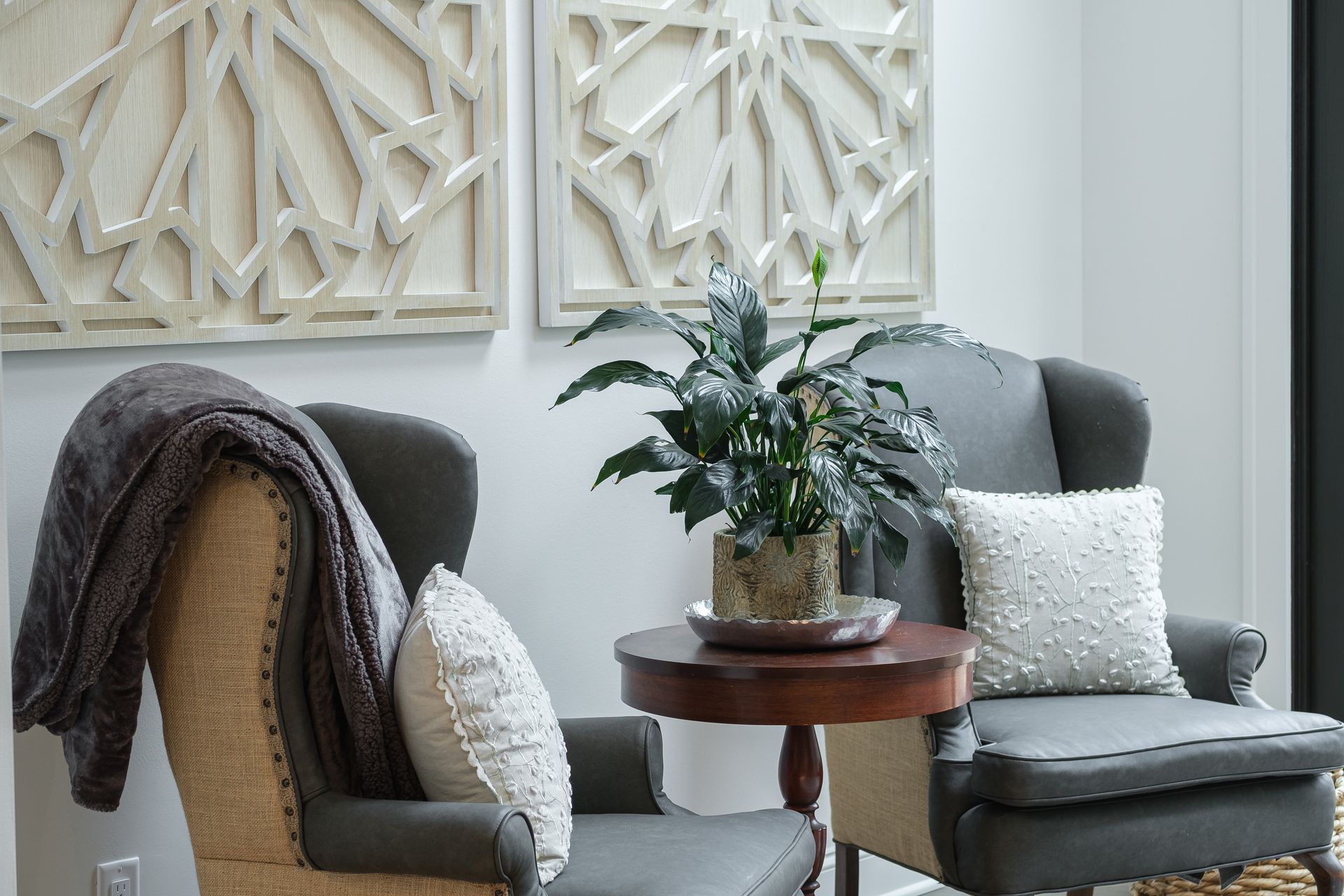 Two gray armchairs with decorative pillows, a table with a plant, and artwork on a white wall.