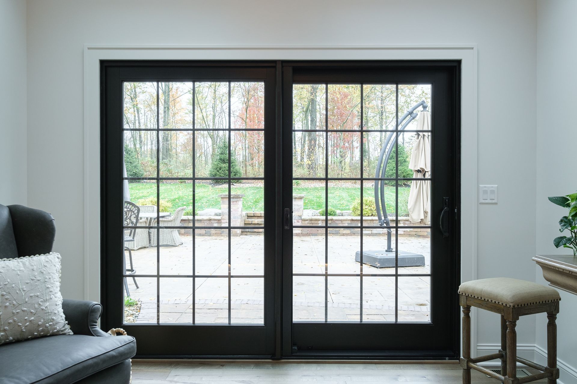 Black grid doors open to a backyard patio, framed by white walls. An armchair and stool sit nearby.