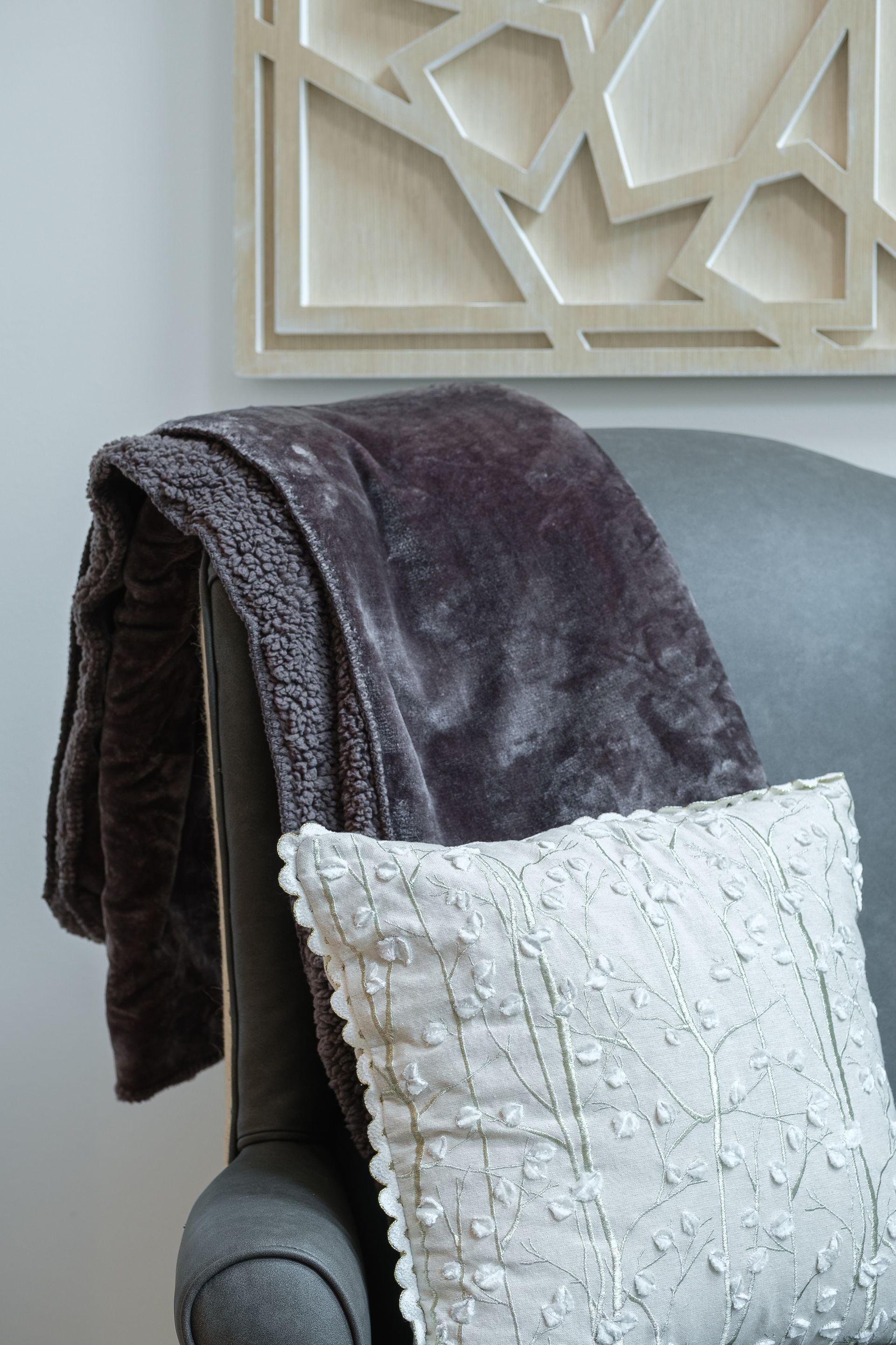 Gray armchair with a fluffy brown blanket and white textured pillow. Geometric wall art.