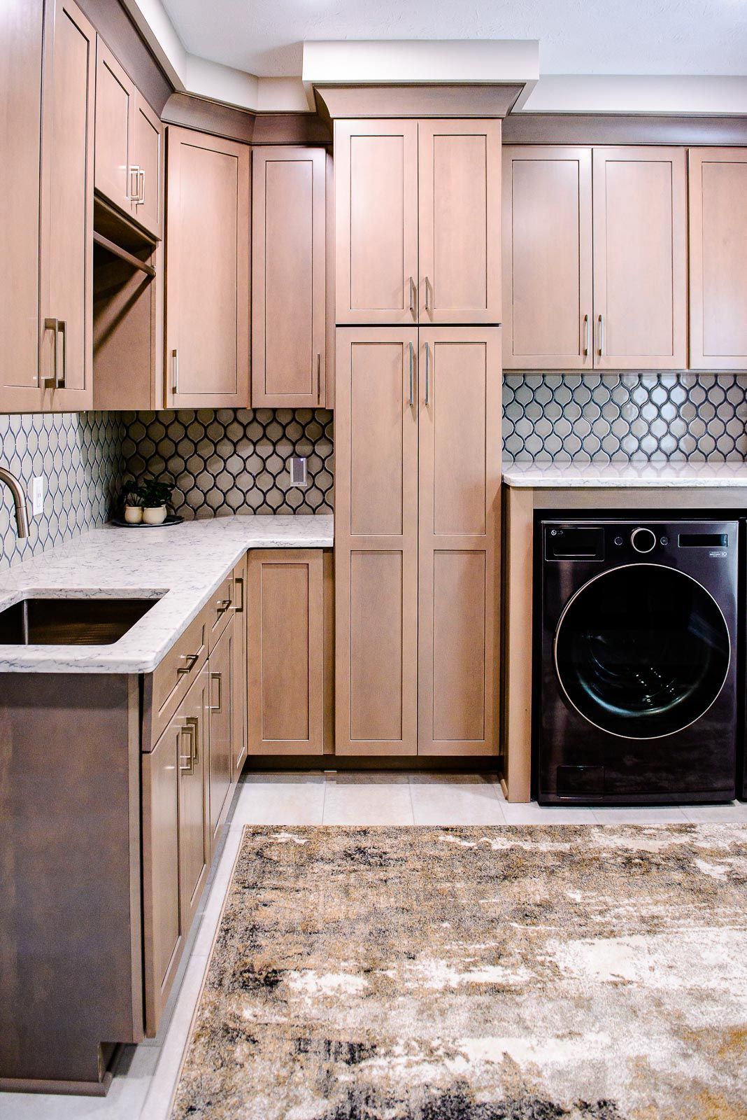 A kitchen with wooden cabinets , a washer and dryer , a sink , and a rug.
