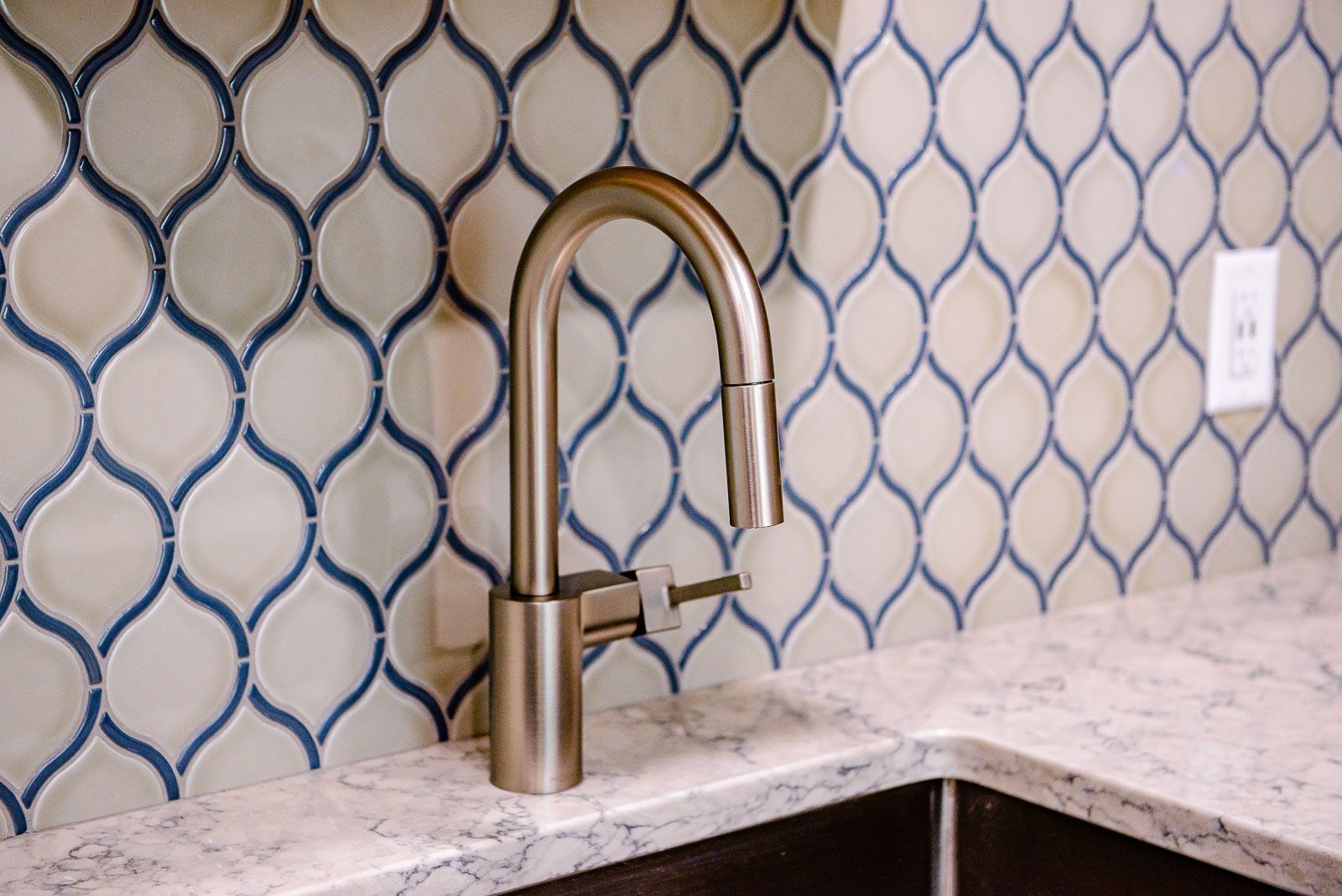 A kitchen sink with a faucet and blue and white tiles on the wall.
