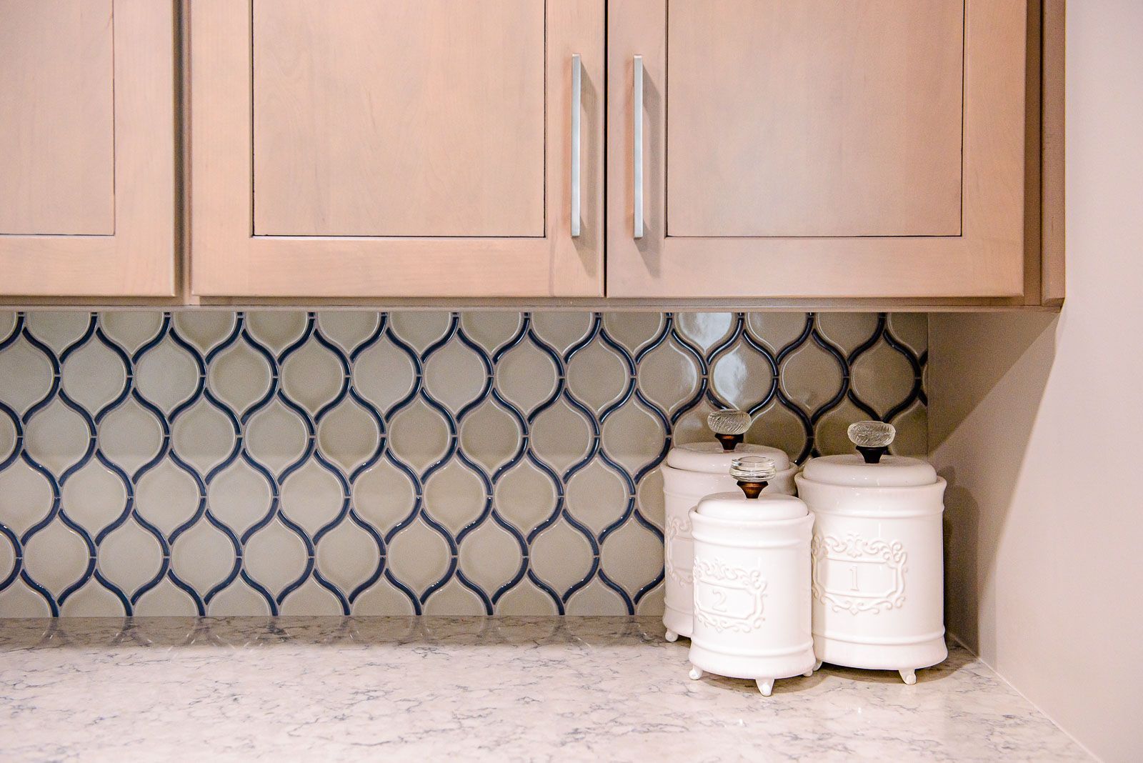 A kitchen with a mosaic tile backsplash and white cabinets.