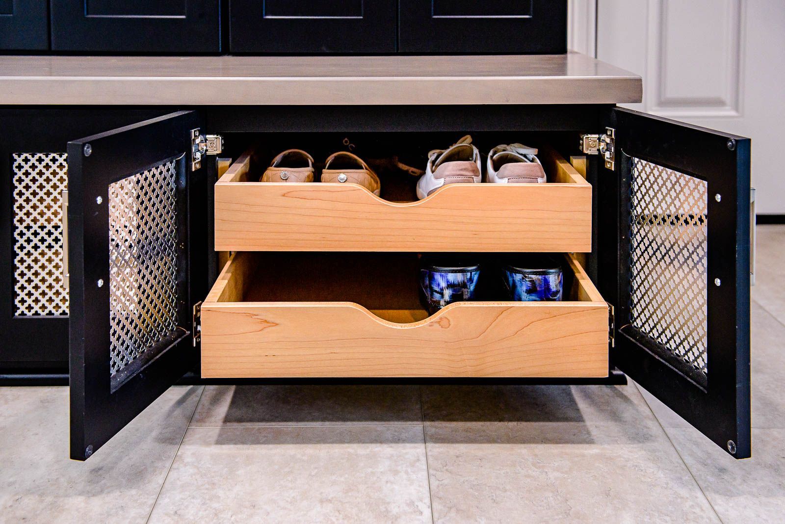 A wooden drawer filled with shoes and bowls in a cabinet.