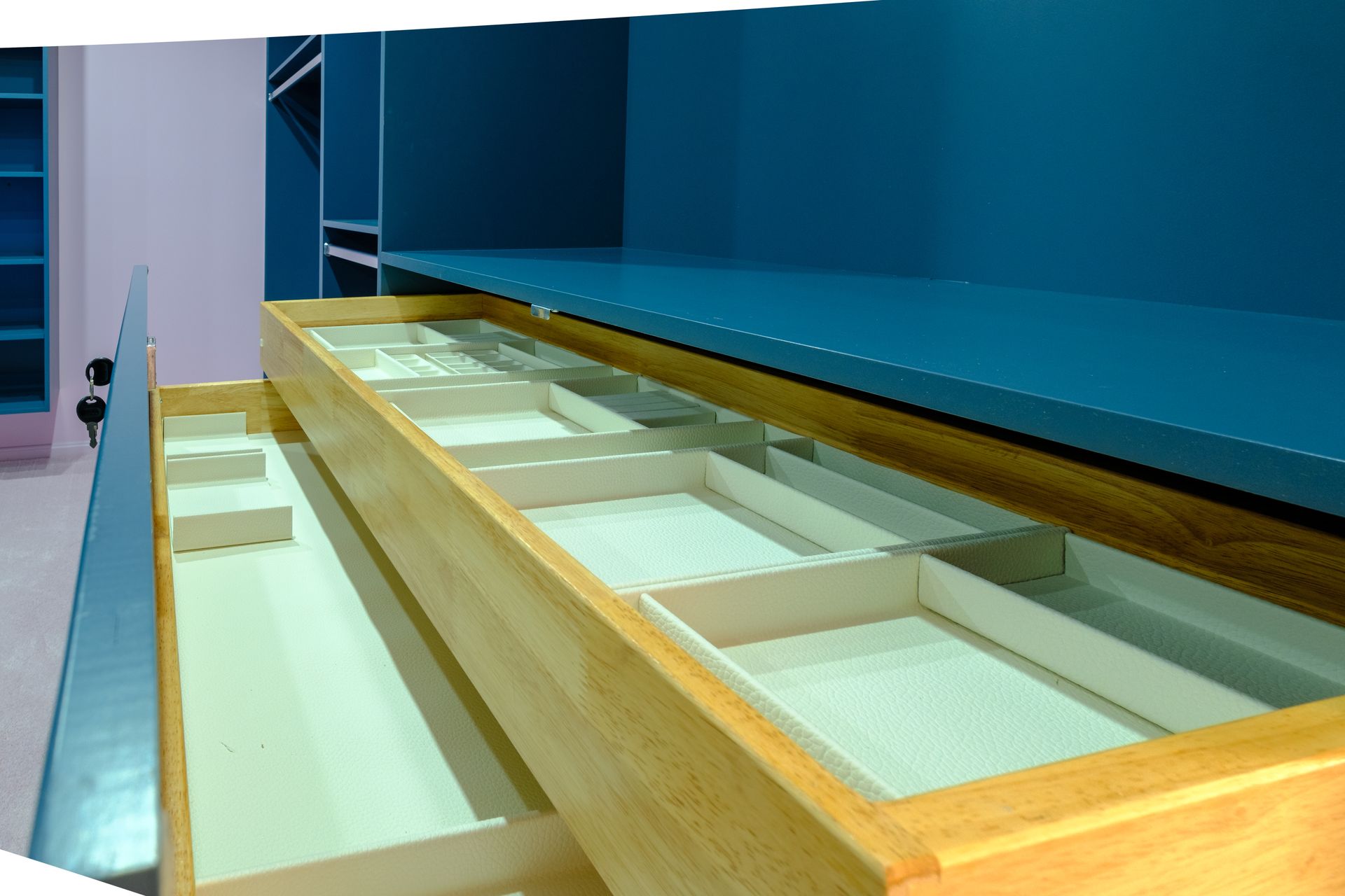 Open wooden drawer with beige dividers, teal cabinet in background.