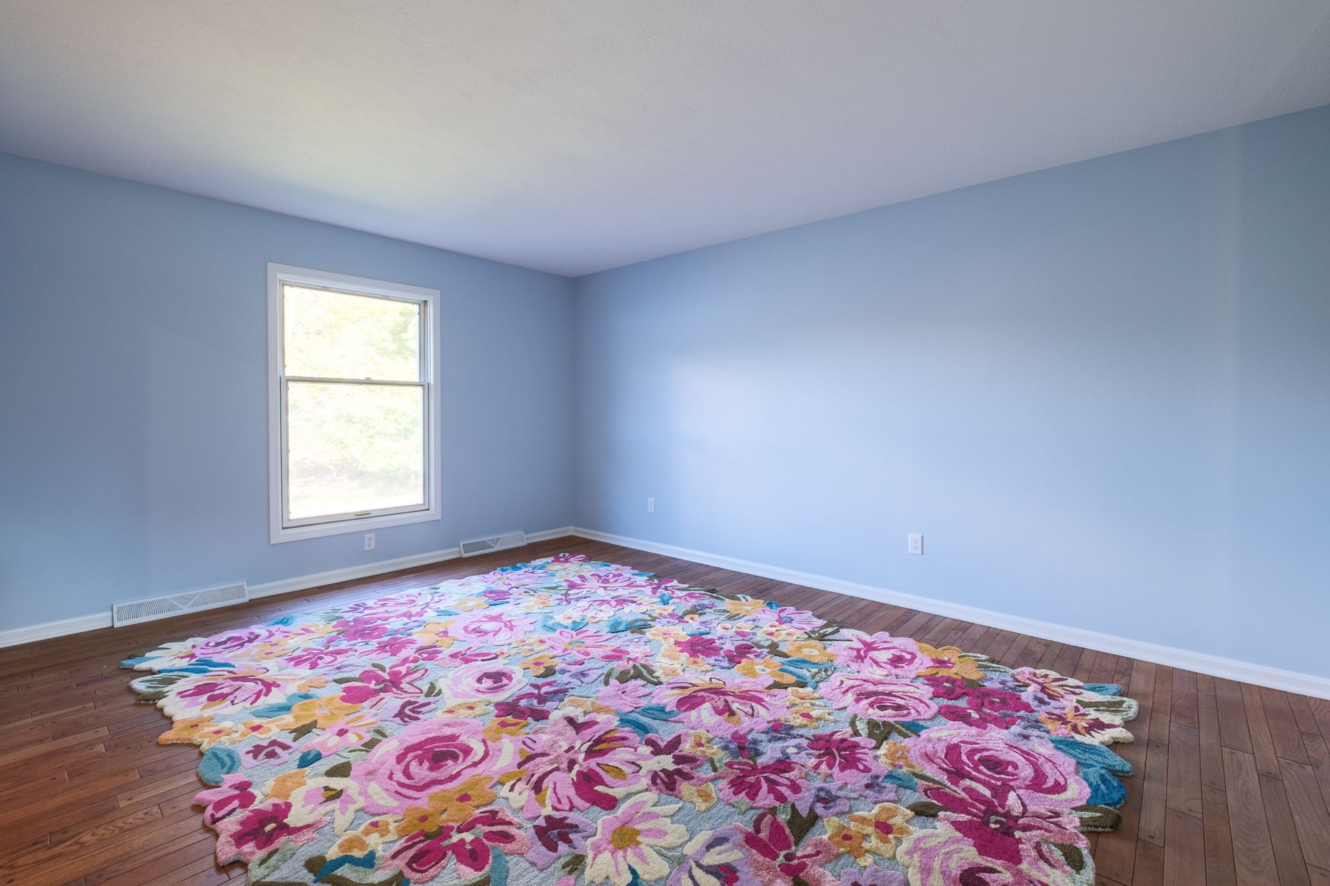 Room with light blue walls, a floral rug, and a window.