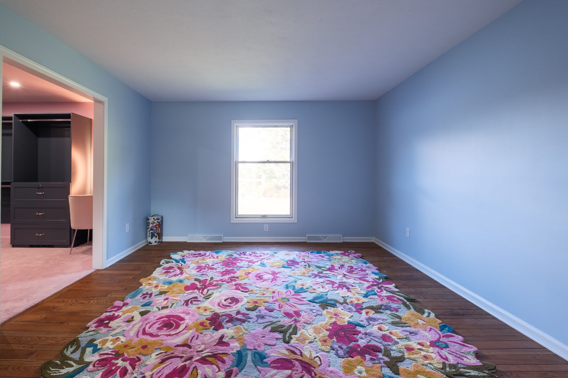 Empty room with blue walls, hardwood floor, floral rug, window, and doorway to a closet.