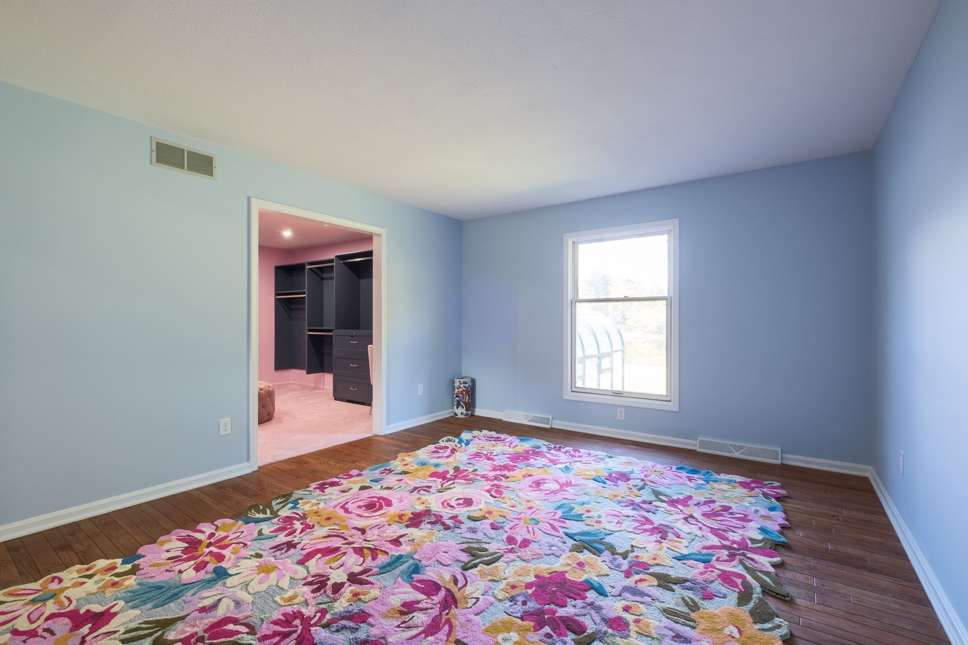 Empty bedroom with blue walls, floral rug, and a walk-in closet.