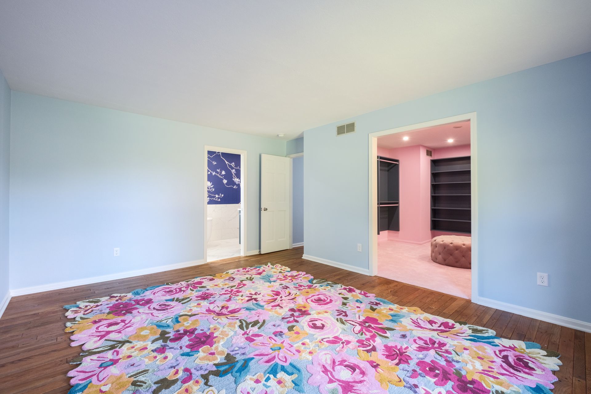 Empty room with floral rug, light blue walls, and a pink-walled walk-in closet.