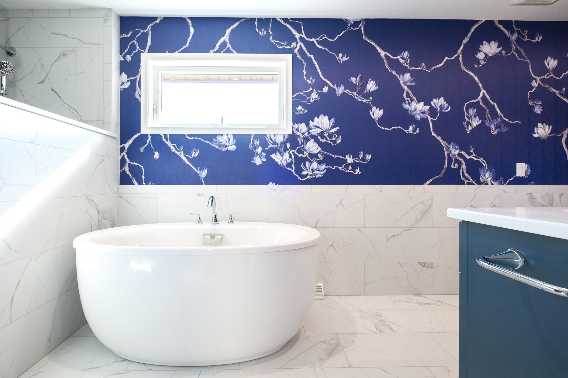 Bathroom with white soaking tub, blue floral wallpaper accent wall, and marble tile.