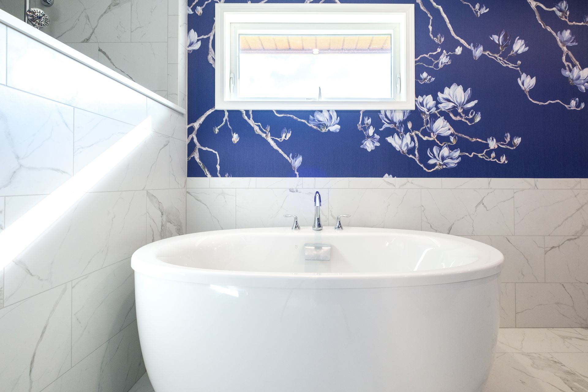 Oval bathtub in a bathroom, with a blue floral patterned wall and a window.