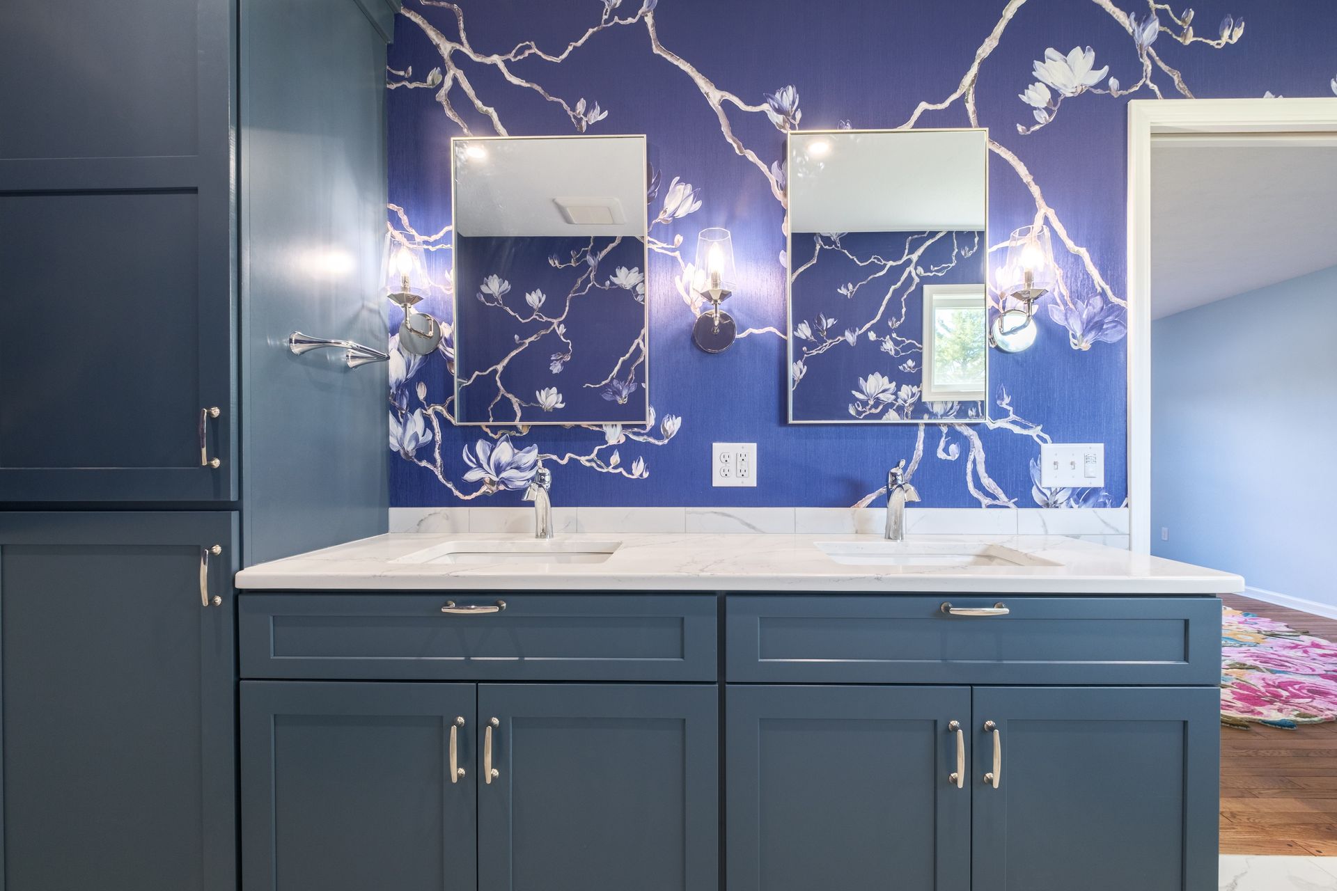 Blue bathroom with floral wallpaper, double sinks, and mirrors.
